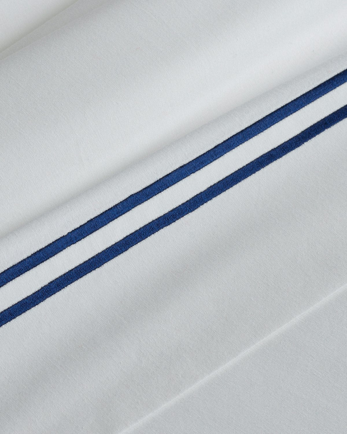Close-up of Petite Plumes Luxe Premium Cotton Sheets in White with Navy, featuring two diagonal navy stripes. Made from long-staple cotton, the fabric is smooth and soft, reminiscent of luxury sheets.