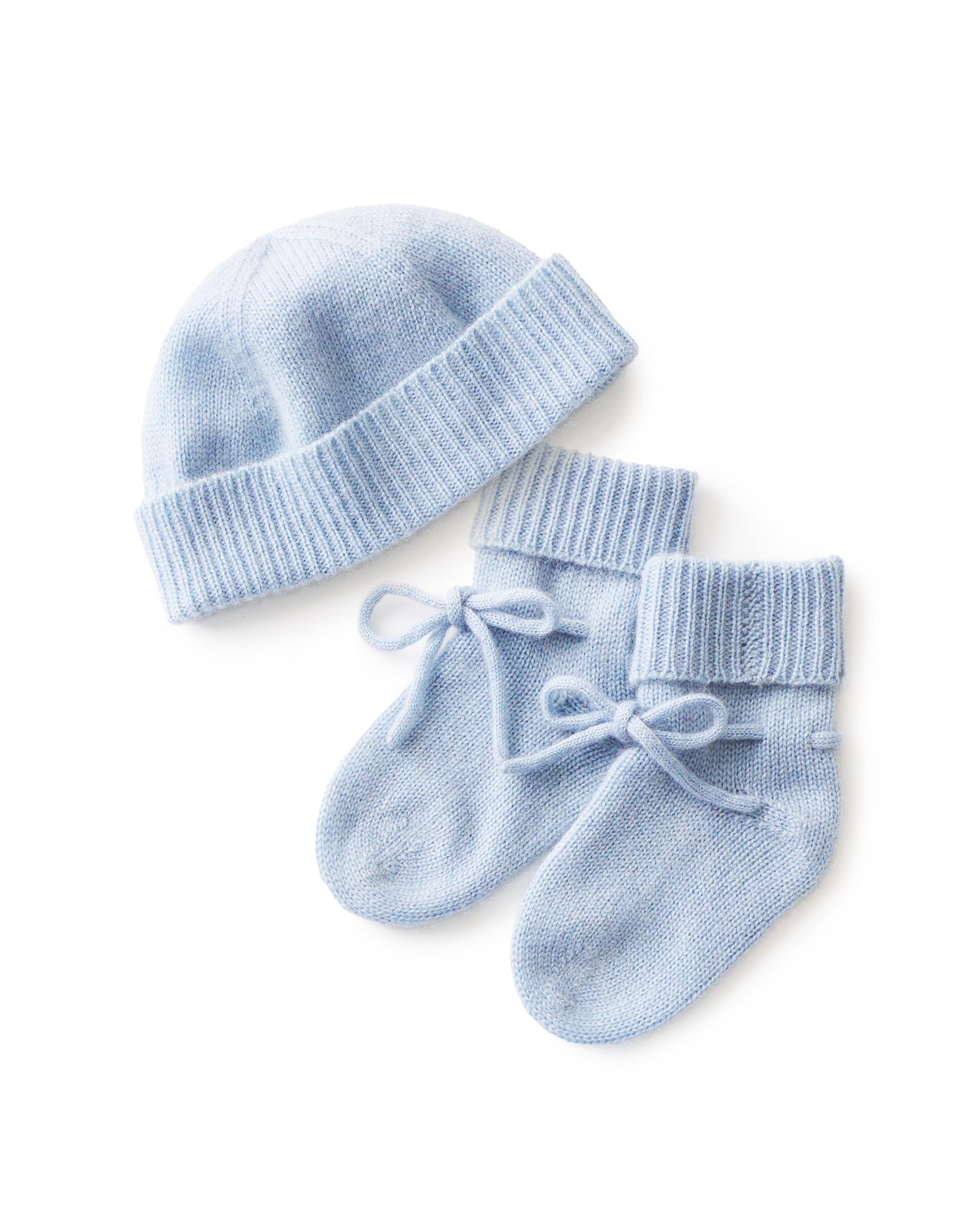 The Baby Cashmere Bootie & Hat Set in Light Blue features a knitted baby hat and matching booties with ribbed cuffs and tied bows, displayed on a white background.