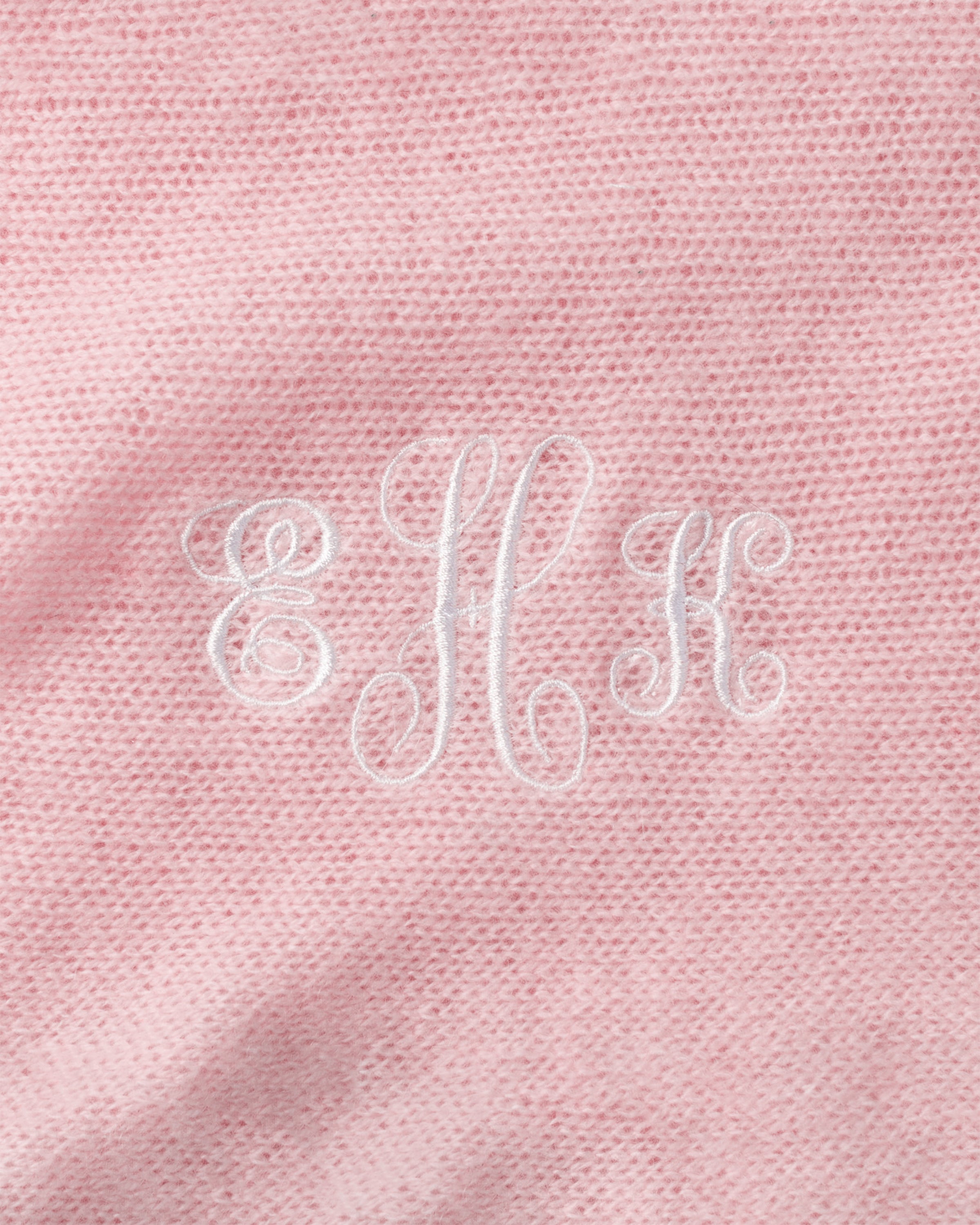The Petite Plume Cashmere Baby Blanket in Rose features pink fabric with embroidered white EHK letters in ornate script. Handmade in Nepal, this luxury gift boasts a subtly textured appearance, epitomizing elegance and warmth.