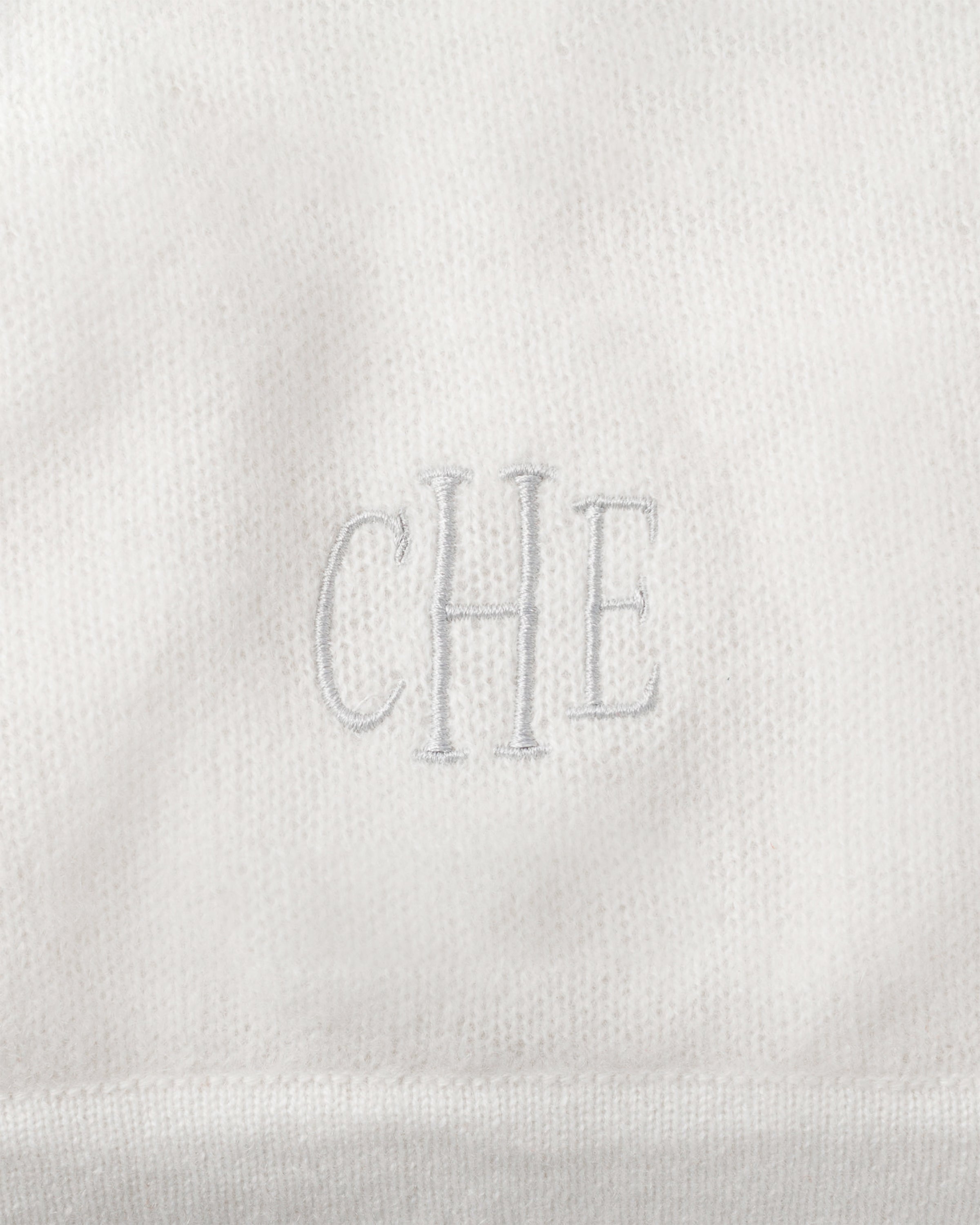 Close-up of Petite Plumes ivory Cashmere Baby Blanket, handmade with CHE embroidered in the center. The soft, slightly fuzzy texture makes it an ideal luxury gift for babies.