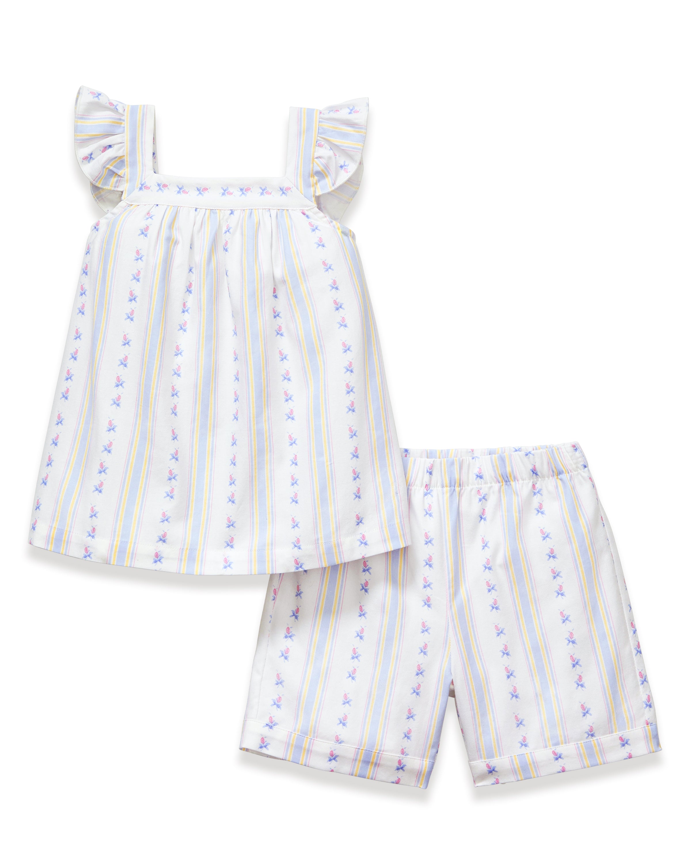 A young girl with curly hair smiles barefoot, wearing the Girl's Twill Clara Short Set in Cottage Stripe— a white sleeveless nightgown and matching shorts—against a plain, light background.