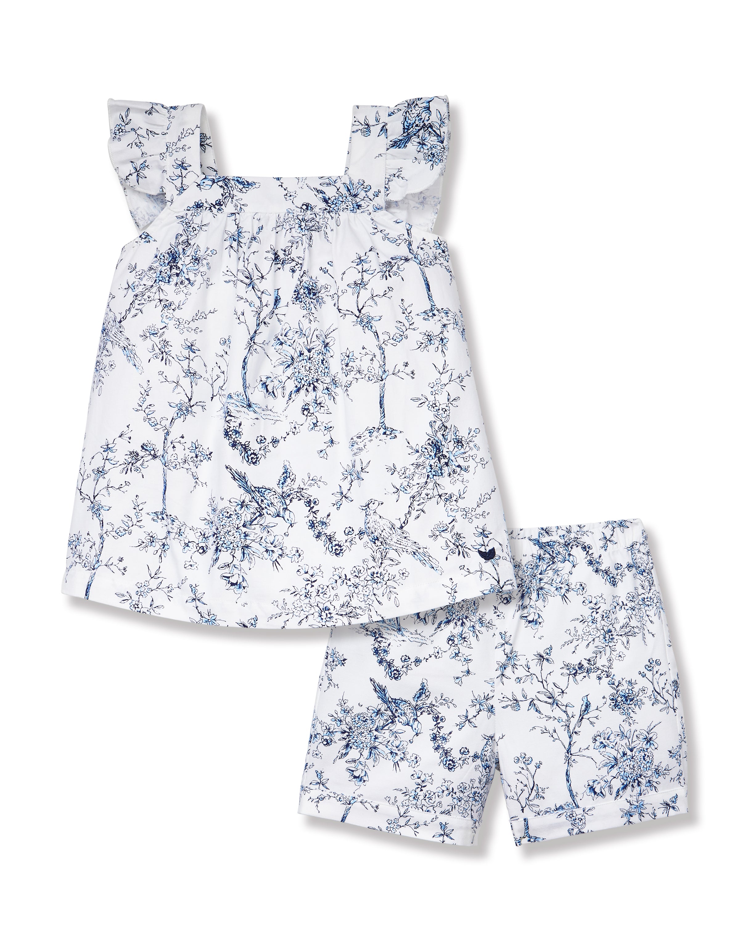 A young girl with long brown hair stands barefoot, smiling in the Girl's Twill Clara Short Set in Timeless Toile—a white top and matching blue floral shorts—posing against a plain light background.