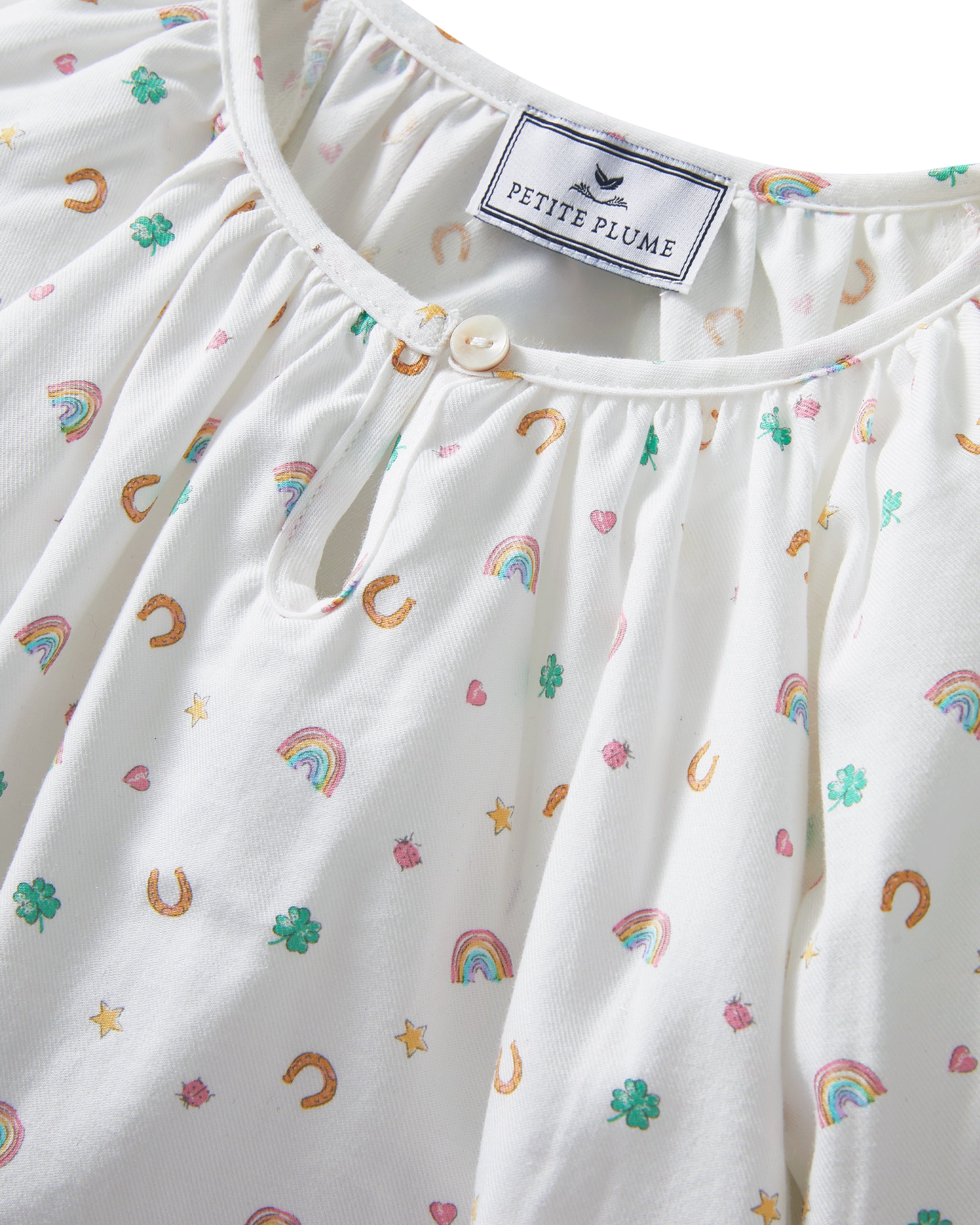 A young girl stands barefoot on a light background, wearing the Girl's Twill Delphine Nightgown in Good Luck Charms. She gazes upward thoughtfully, showcasing its long sleeves and colorful pattern.