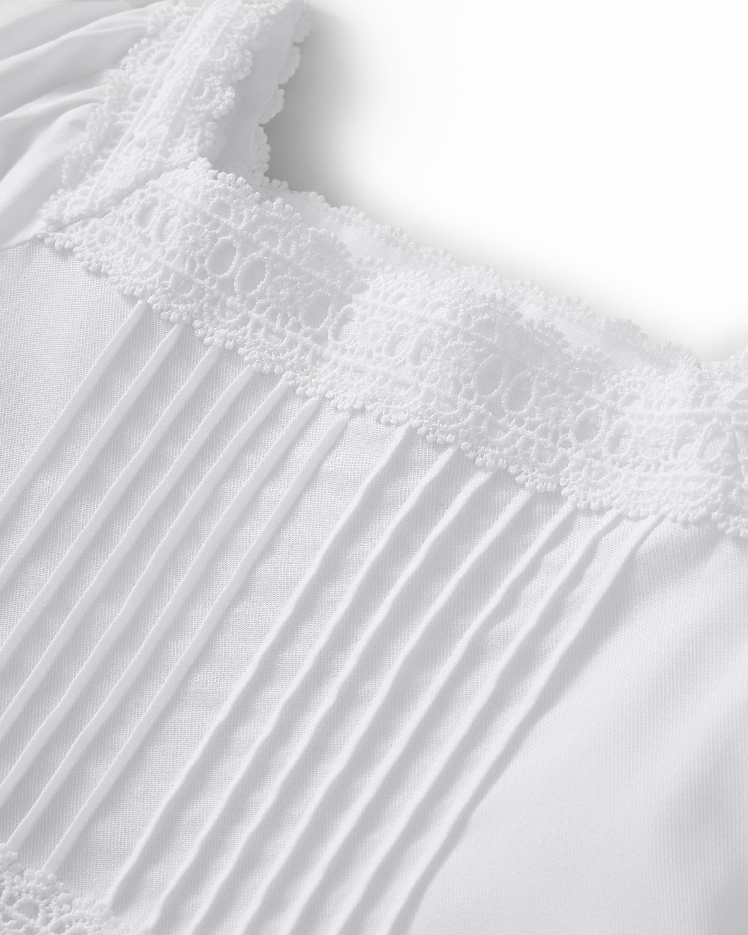 A young girl stands barefoot against a light background, wearing the Girl's Twill Juliette Nightgown in White—a knee-length piece with short sleeves, lace trim, and pintuck details. She gazes gently to the side.