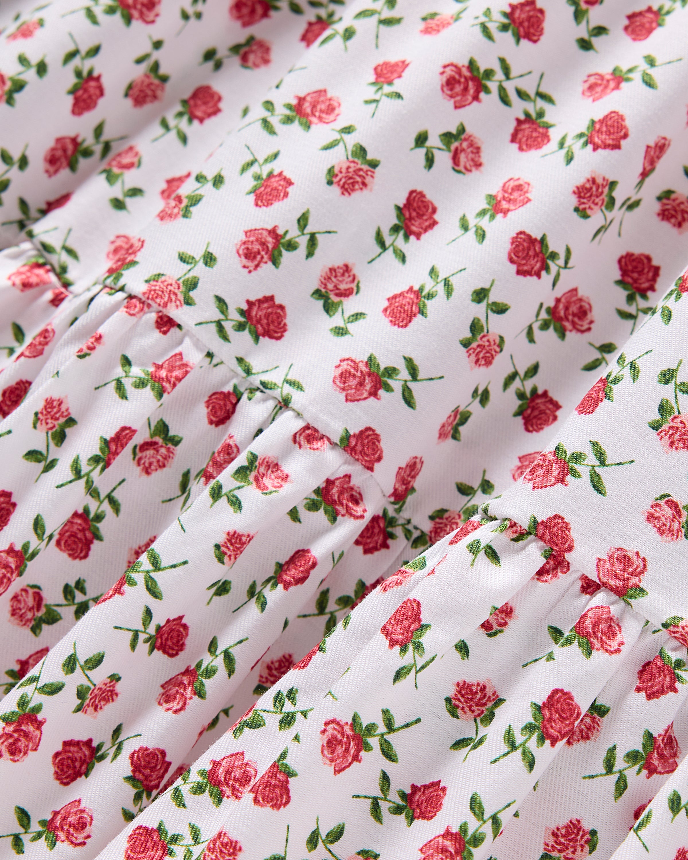 Close-up of the Girls Lily Nightgown in Petite Petals by Petite Plume, crafted from yarn-dyed cotton with a small red roses and green leaves pattern on white. The material is slightly gathered for a textured, luxurious sleepwear experience.