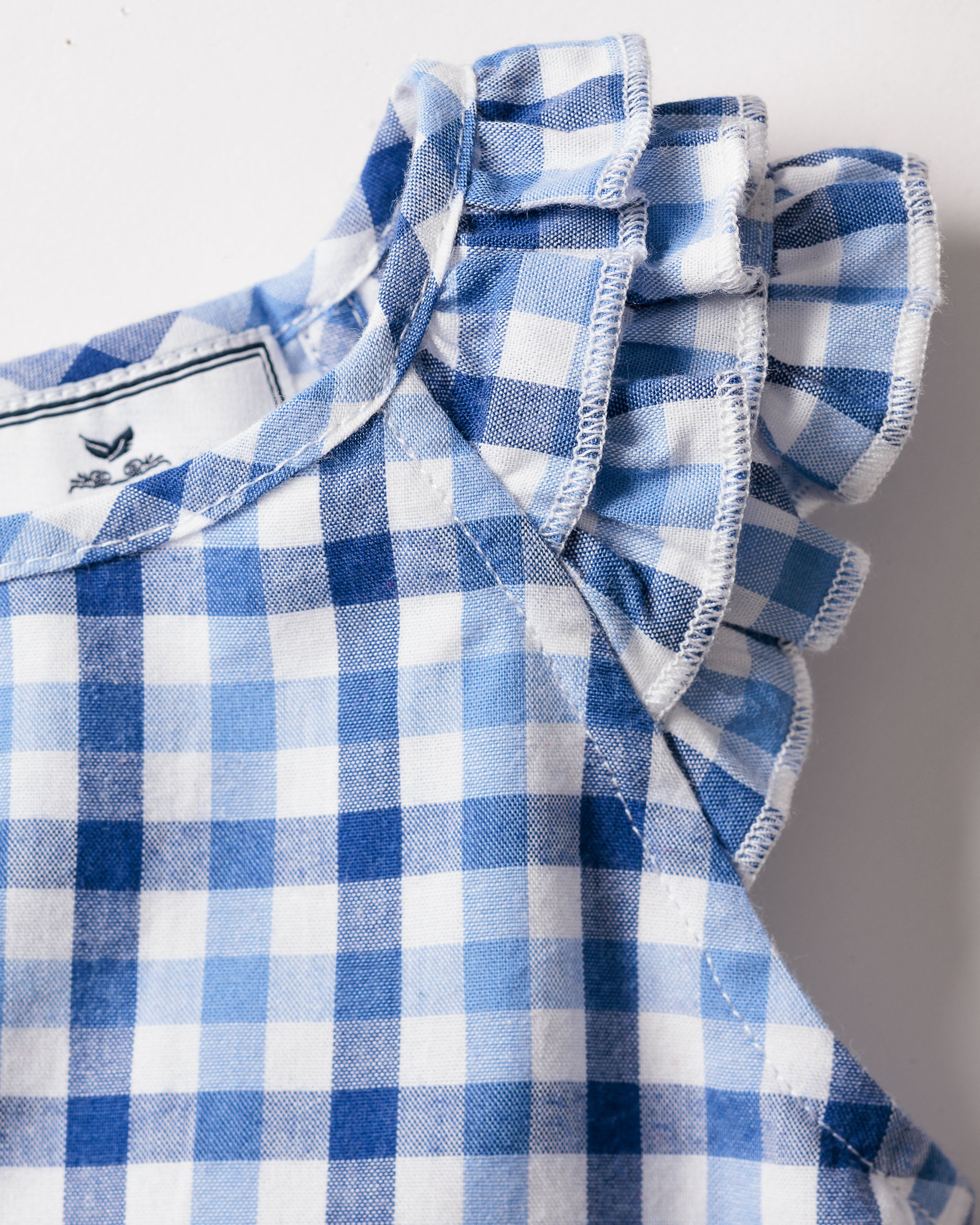 Close-up of a Petite Plume girls twill Amelie nightgown in royal blue gingham print, with ruffled edges and a visible tag inside. The sleepwear showcases stitching details and features alternating shades of blue in its classic check pattern.