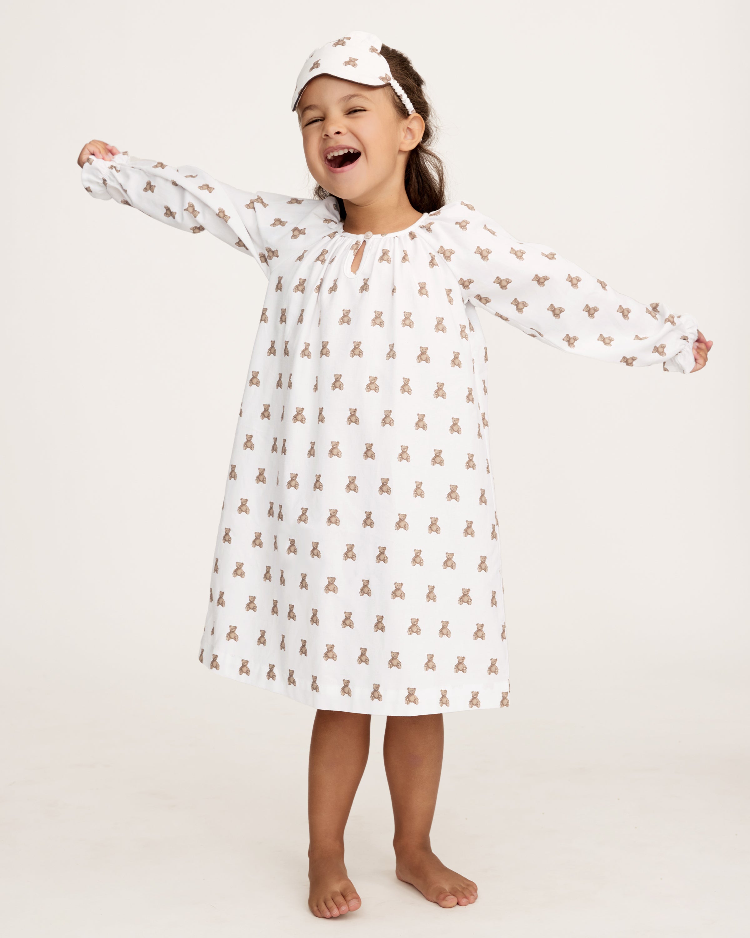 The Girl's Twill Delphine Nightgown in Teddy Tales features long sleeves, a white fabric with an all-over brown teddy bear print, a gathered neckline, ruffled cuffs, and a button closure at the collar.