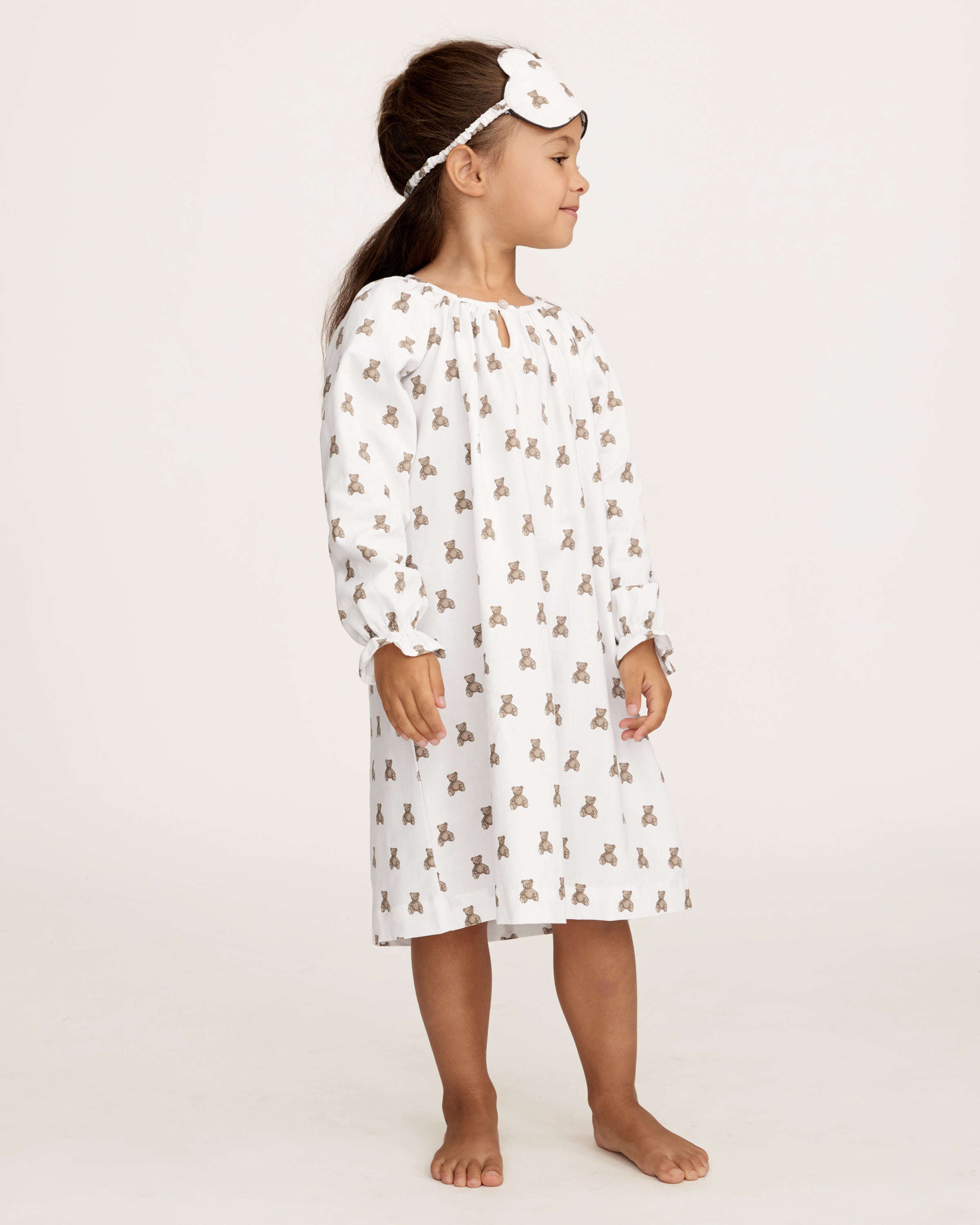 The Girl's Twill Delphine Nightgown in Teddy Tales features long sleeves, a white fabric with an all-over brown teddy bear print, a gathered neckline, ruffled cuffs, and a button closure at the collar.