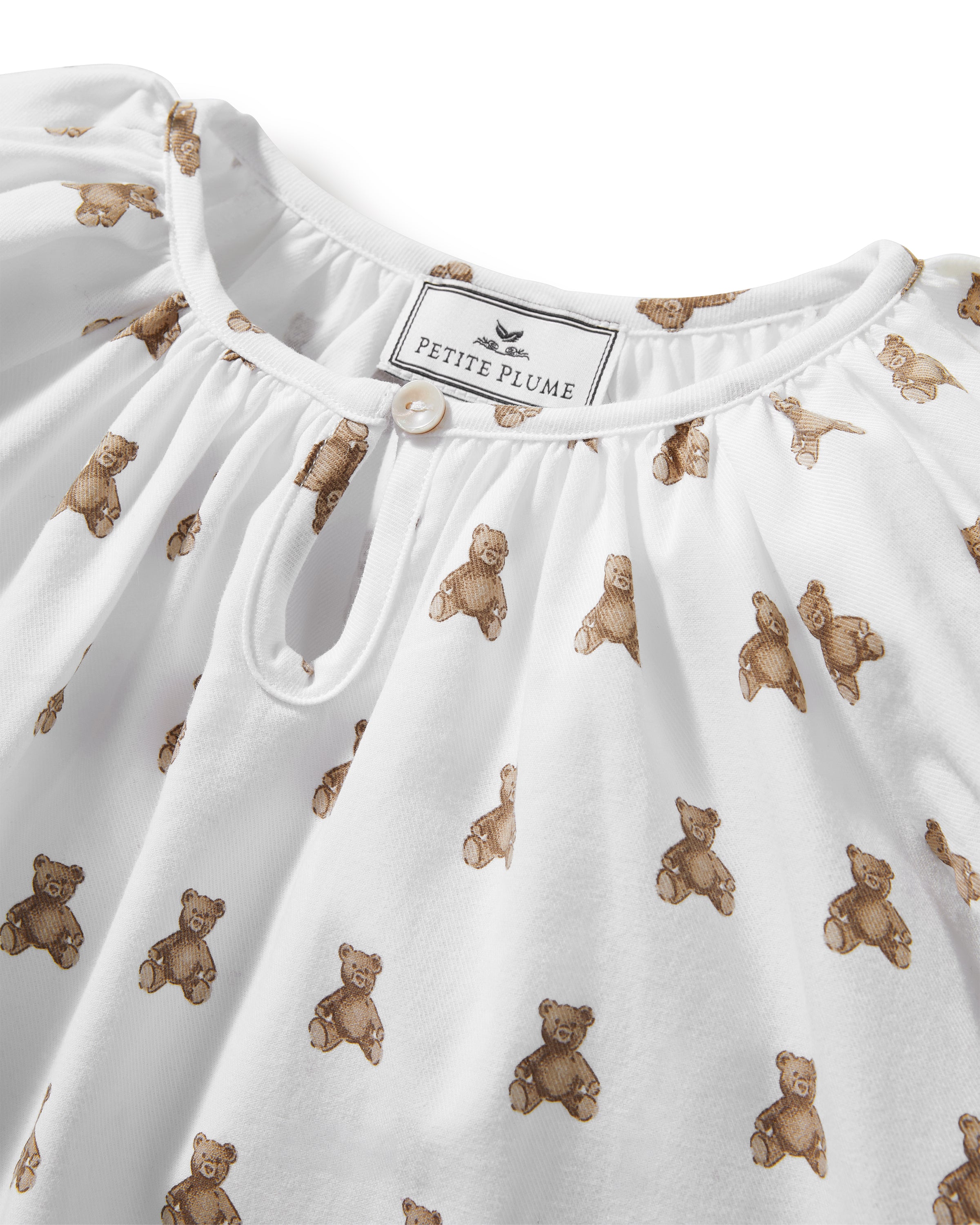 The Girl's Twill Delphine Nightgown in Teddy Tales features long sleeves, a white fabric with an all-over brown teddy bear print, a gathered neckline, ruffled cuffs, and a button closure at the collar.