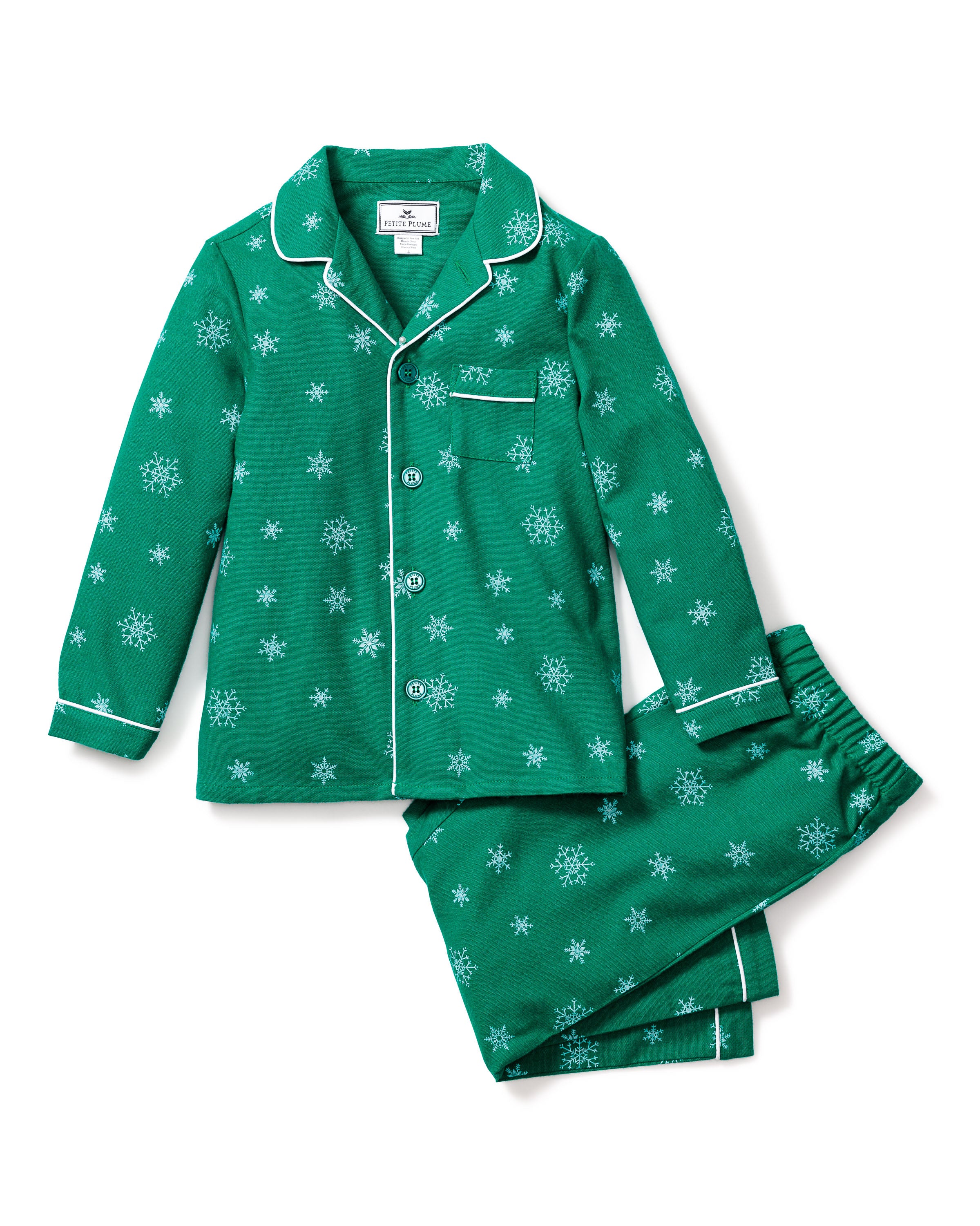 The Kids Flannel Pajama Set in Emerald Wonderland by Petite Plume features a moisture-wicking twill design with a long-sleeve top and pants adorned with white snowflakes. The top includes white piping, buttons, and a chest pocket, while the pants have an elastic waistband for comfort.