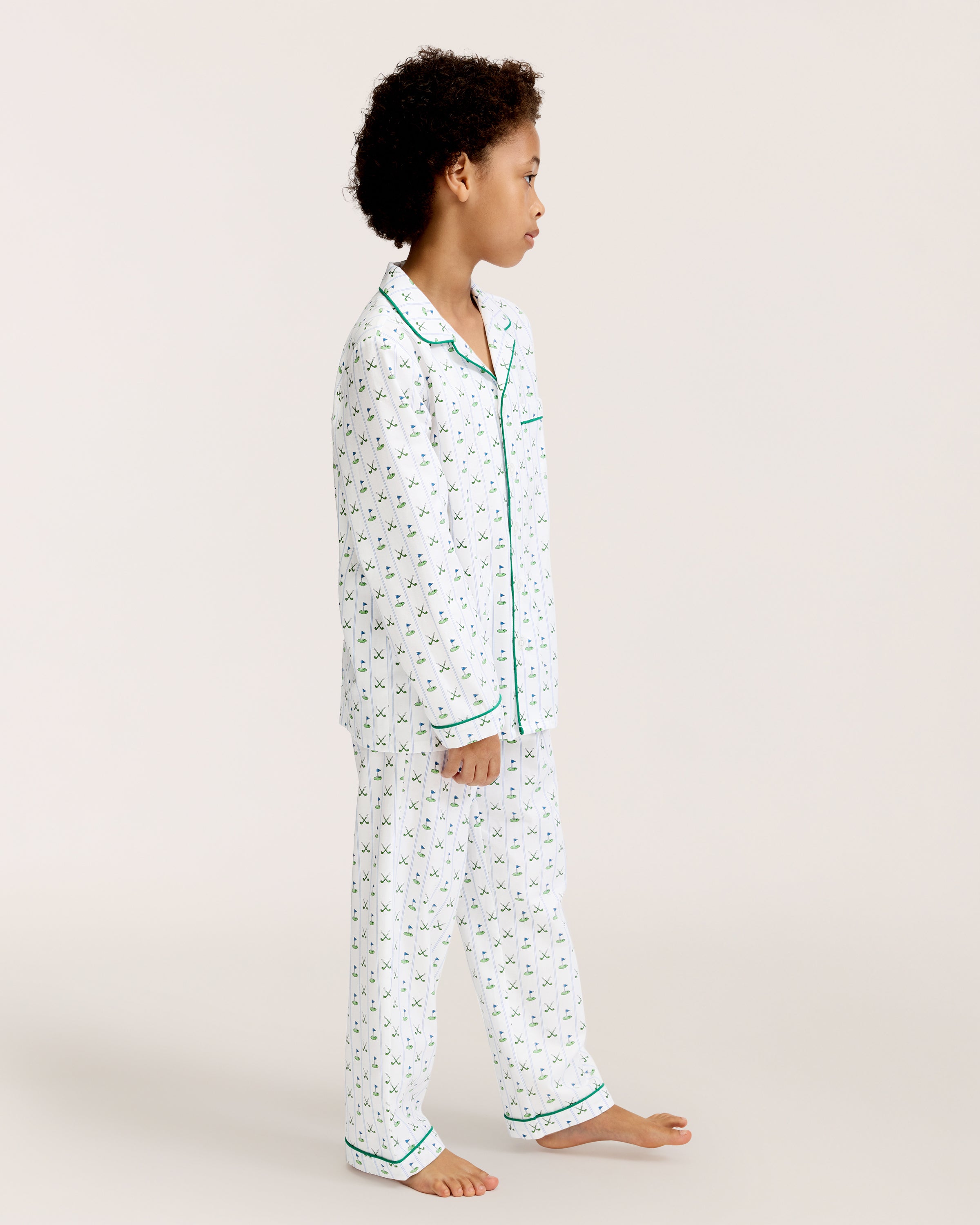 The Kid's Twill Pajama Set in Fairway Stripe features white pajamas with green piping, a tennis racket and green stripe pattern, a long-sleeve button-up top with a chest pocket, and matching long pants.