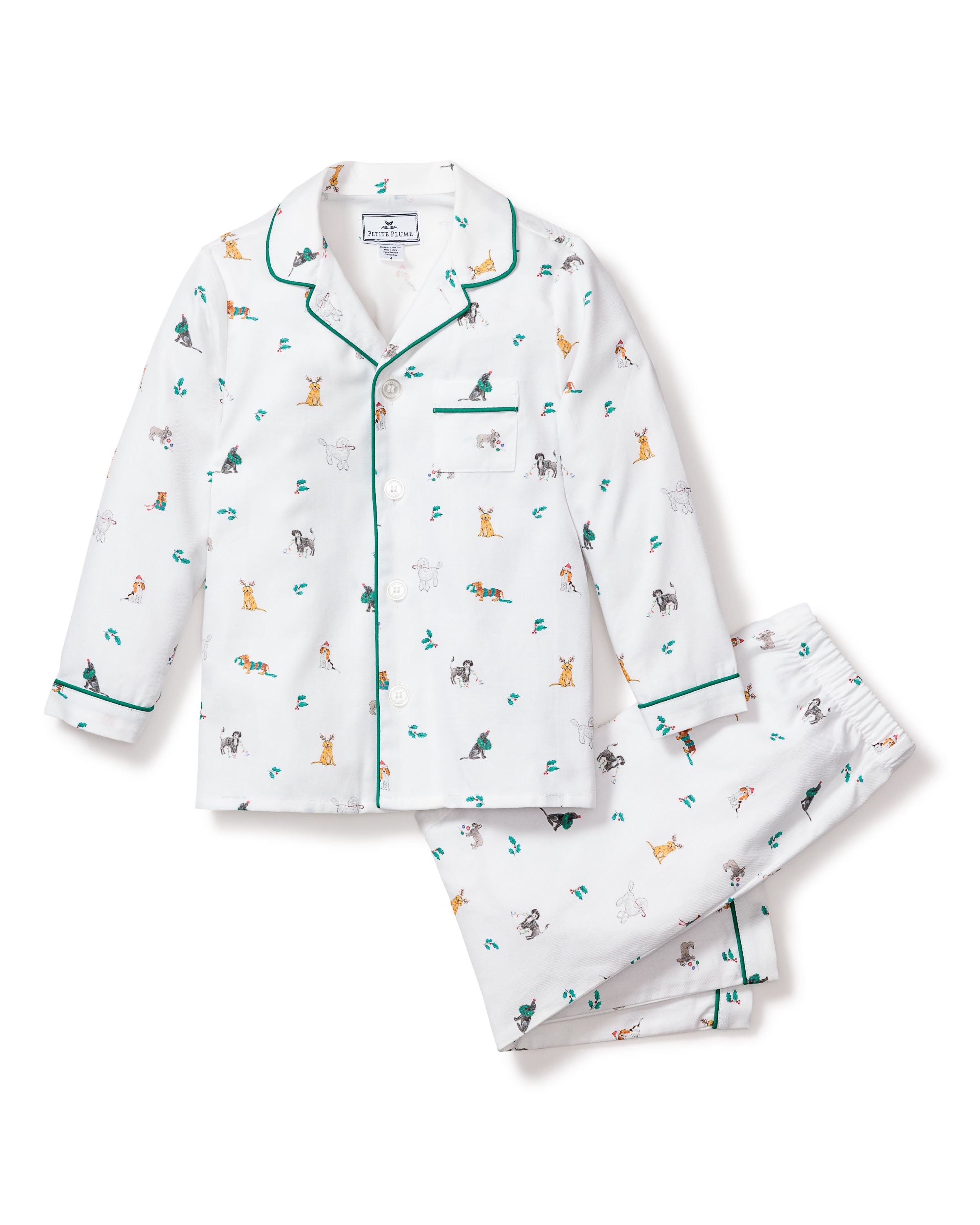 The Kids Twill Pajama Set in Jingle Paws by Petite Plume is a festive two-piece white ensemble featuring multicolored cartoon dog prints. It includes a long-sleeved, button-up top with a chest pocket and matching pants, both adorned with dark green piping on the edges.