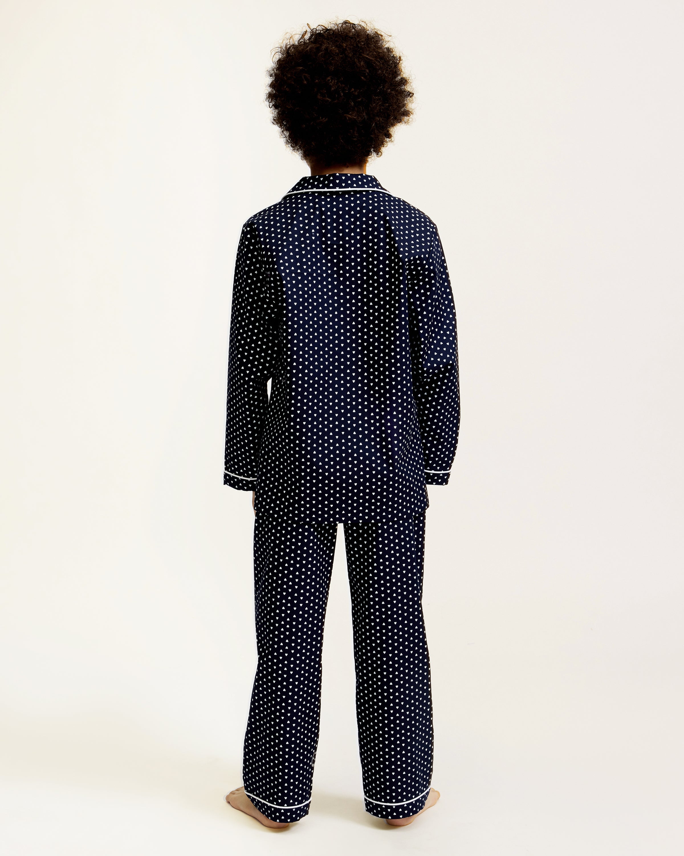 Kid's Twill Pajama Set in Midnight Hearts features navy blue pajamas with white heart prints, white piping, a long-sleeve button-up top with chest pocket, and matching pants.