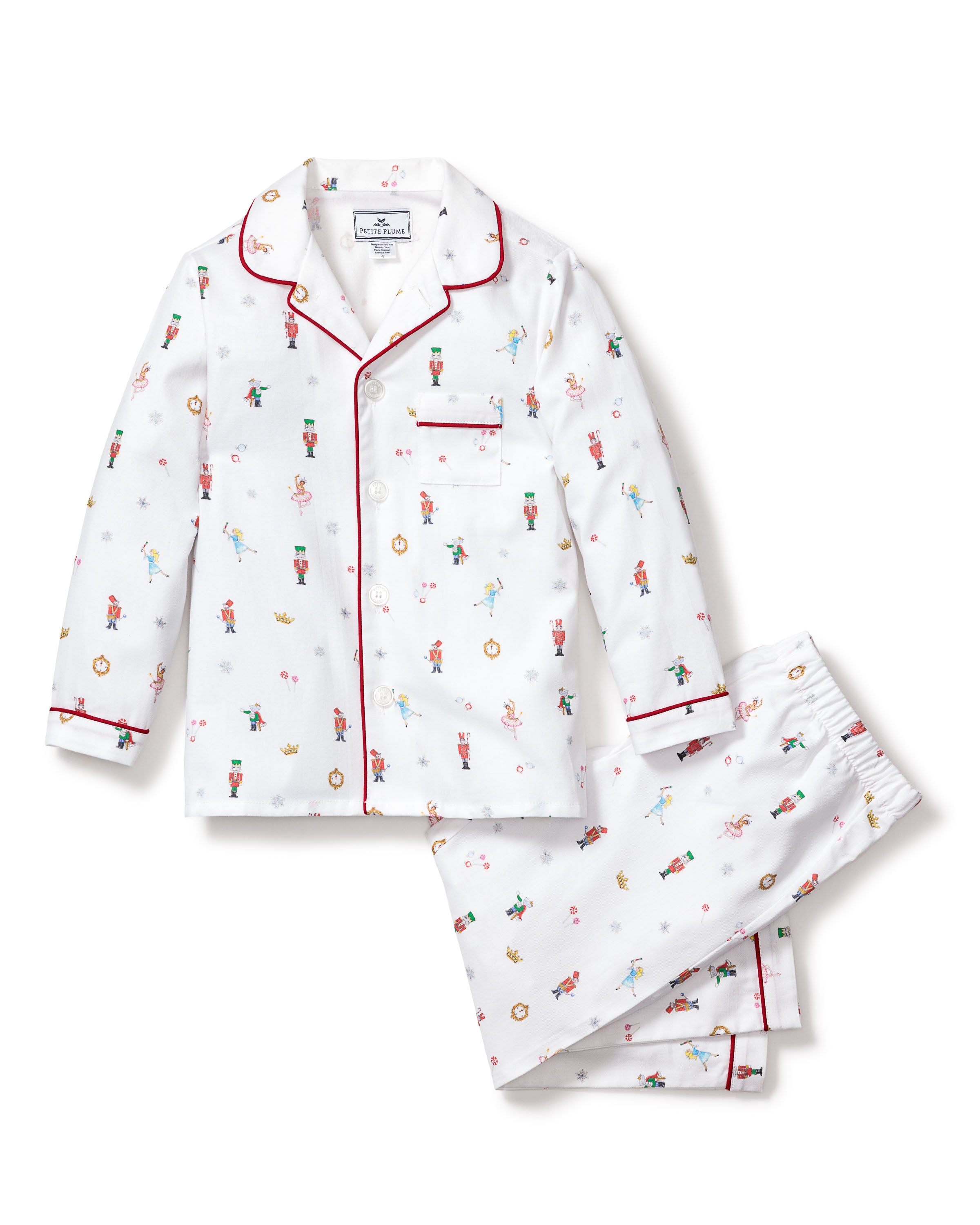 The Kids Twill Pajama Set in A Night at the Nutcracker by Petite Plume features playful, white childrens sleepwear with colorful elves and Christmas ornaments. This set includes a collared, long-sleeve top with a pocket and matching pants, highlighted by red piping for festive charm.