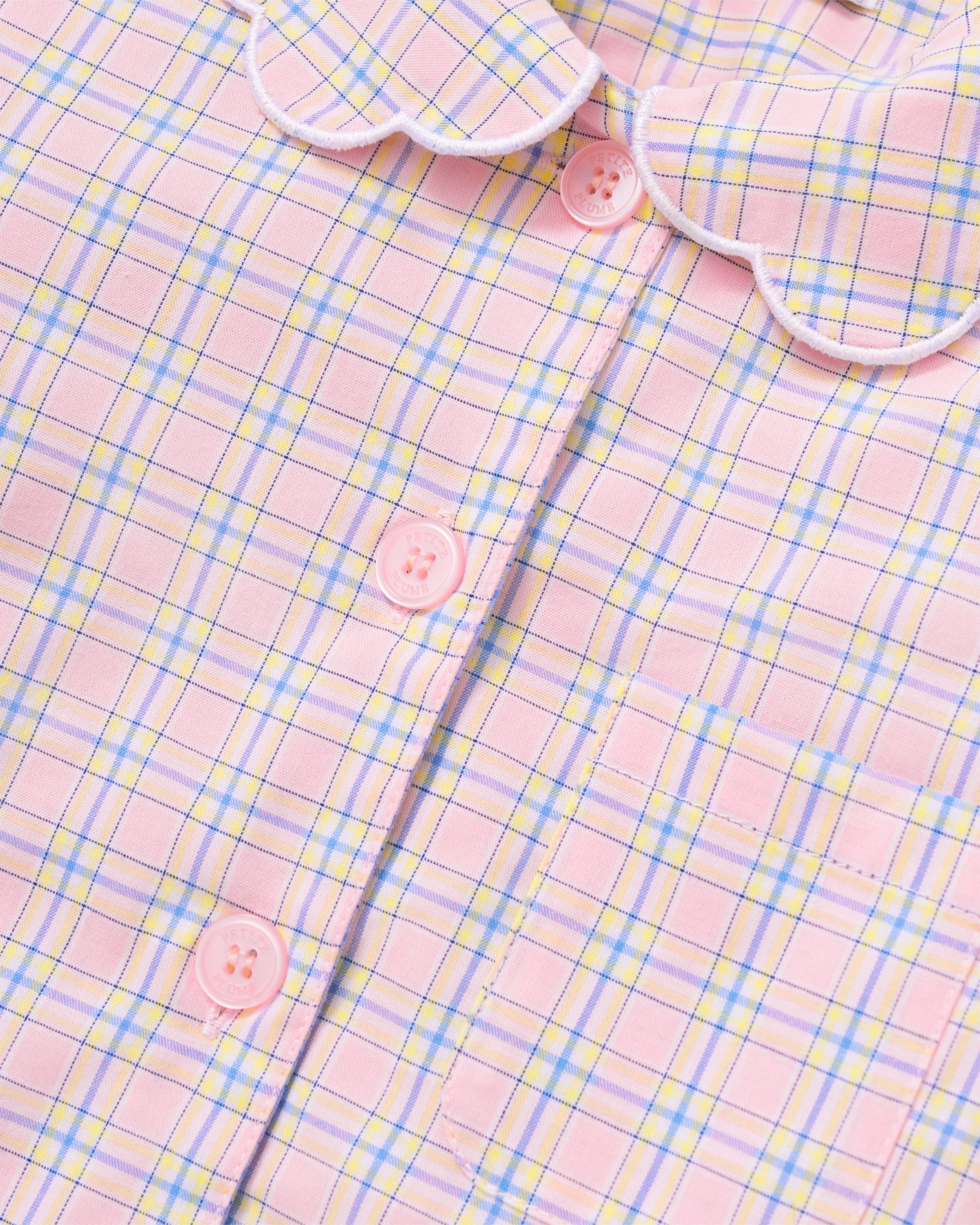 Young girl with long blonde hair wears the Kid's Twill Colette Pajama Set in Peony Plaid, featuring pink and white checks, scalloped edges, and stands barefoot against a plain light background.