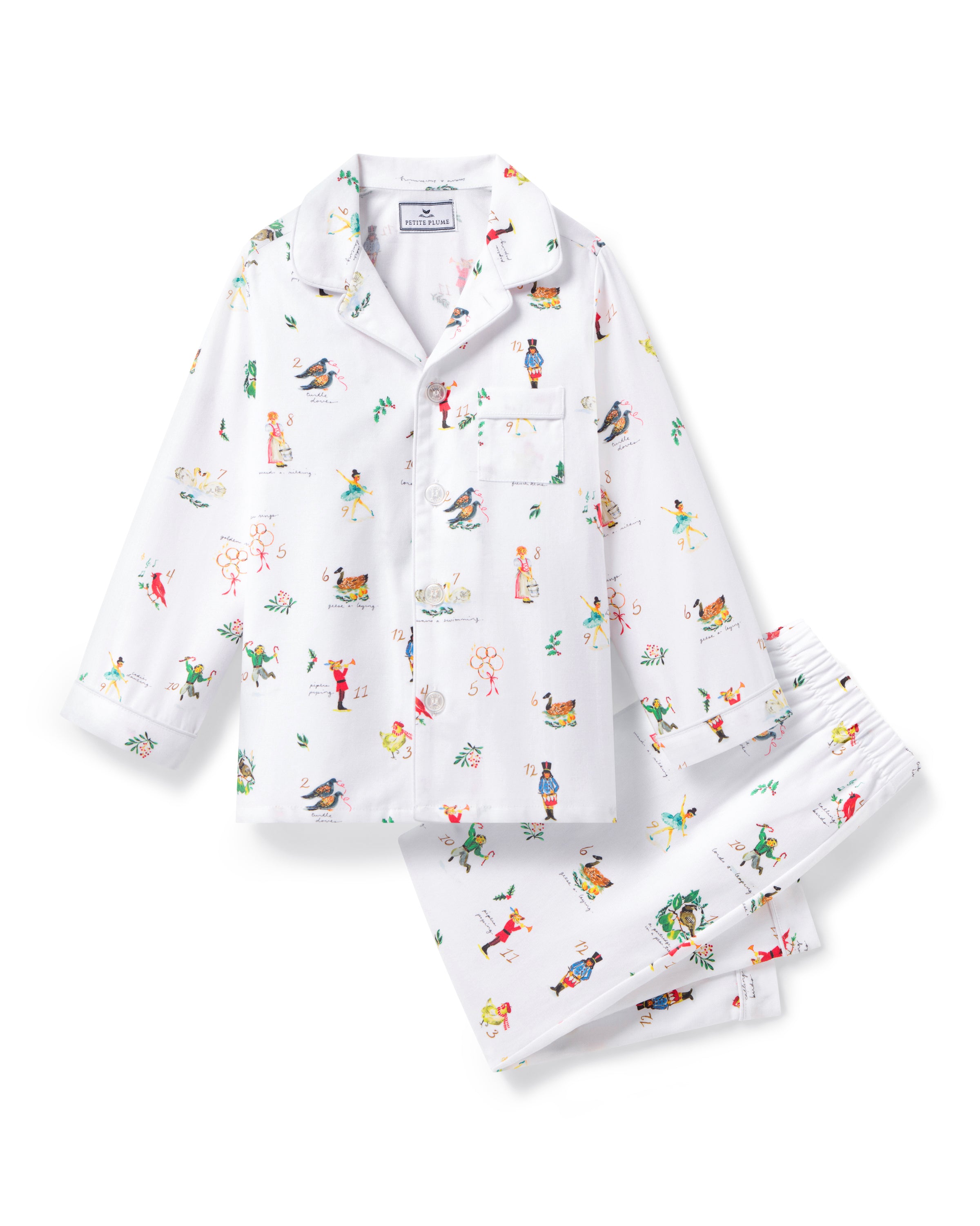 The Kid's Twill Pajama Set in 12 Days of Christmas features a white, long-sleeve button-up top with collar and front pocket, plus matching pants, all adorned with playful, colorful holiday illustrations of people and animals.