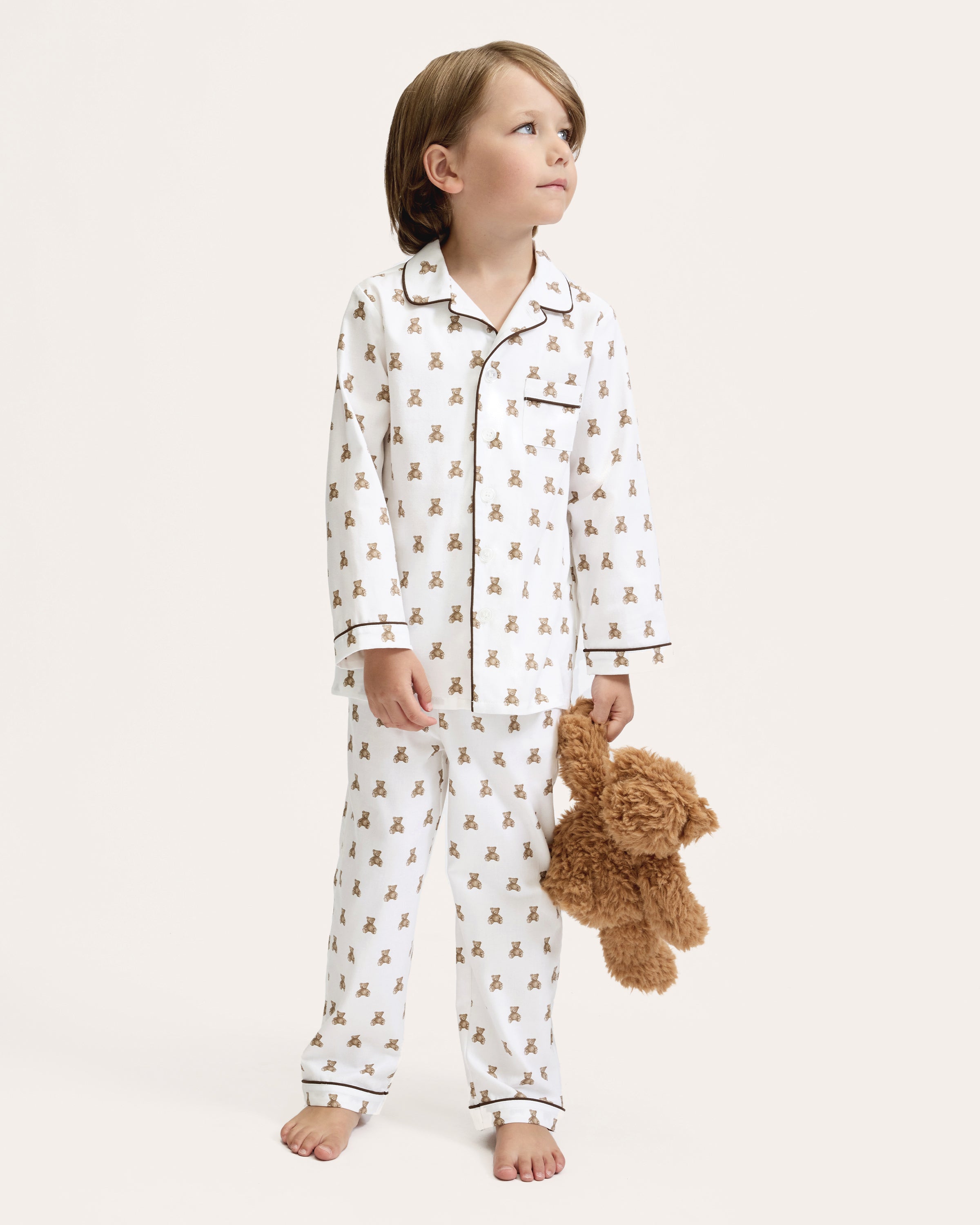 Kid's Twill Pajama Set in Teddy Tales: white long-sleeve, button-up pajamas with pants, featuring brown teddy bear print, dark piping along edges and chest pocket.