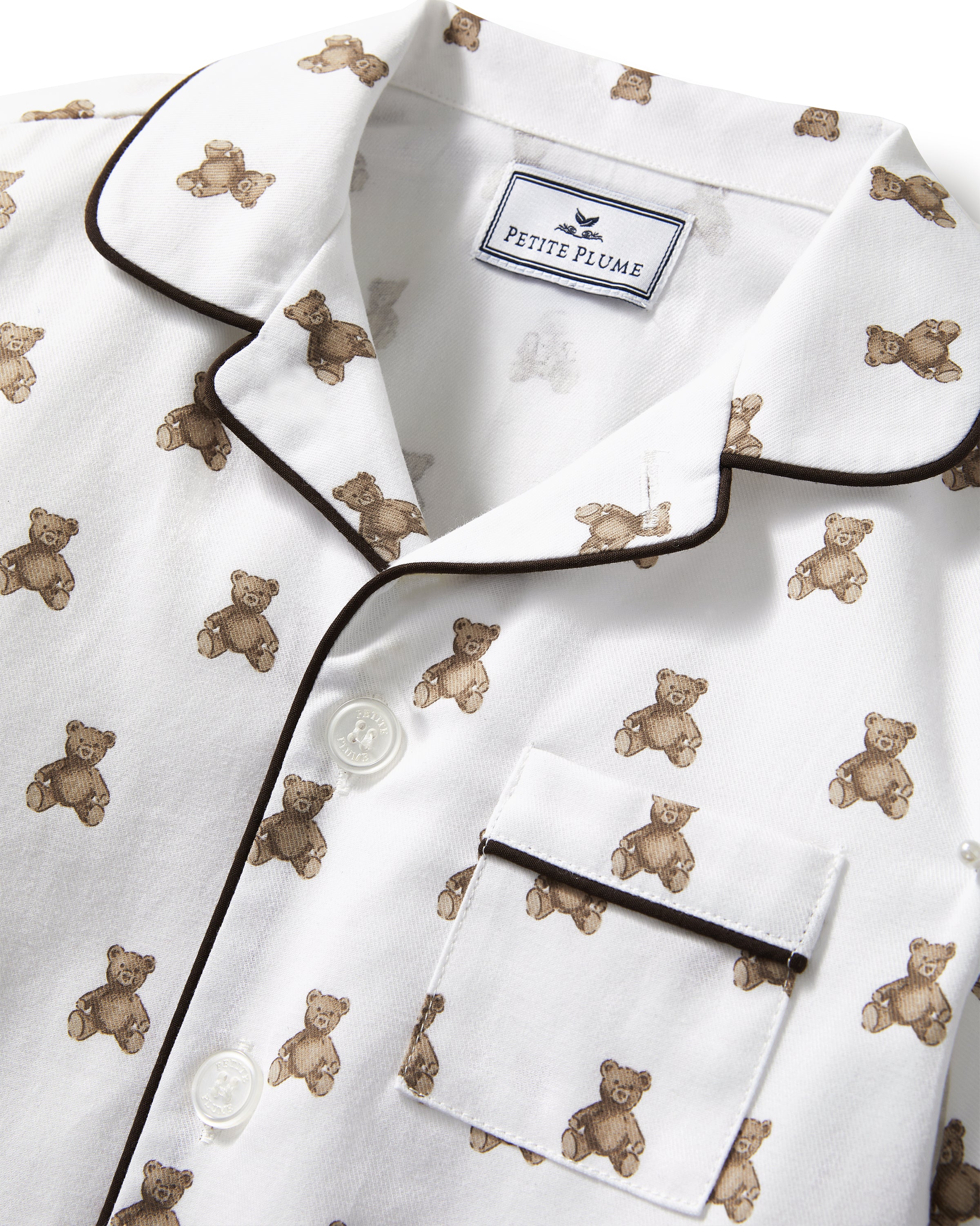 Kid's Twill Pajama Set in Teddy Tales: white long-sleeve, button-up pajamas with pants, featuring brown teddy bear print, dark piping along edges and chest pocket.