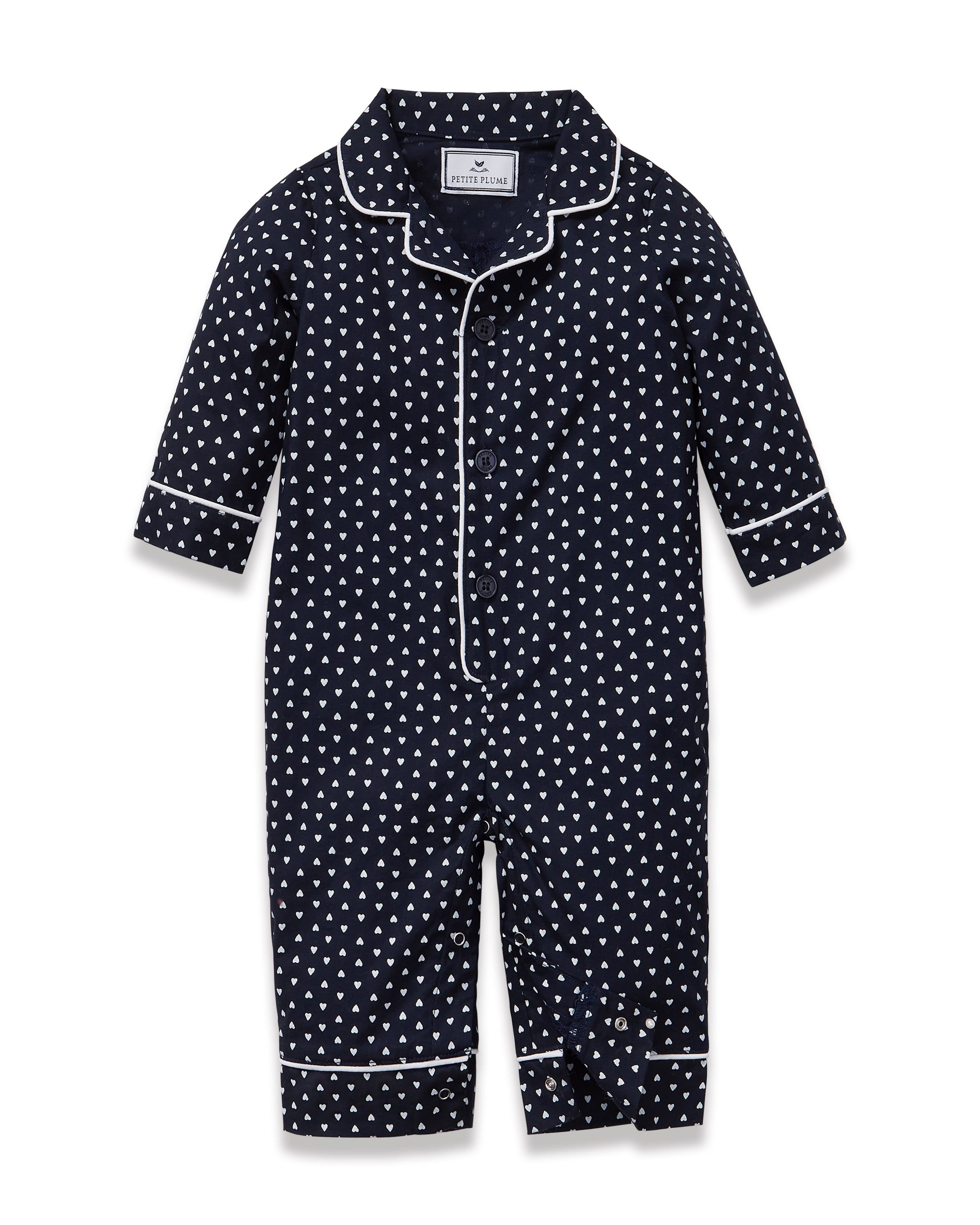 The Baby's Twill Classic Romper in Midnight Hearts is a navy blue onesie with long sleeves and legs, featuring a white heart pattern and white piping on the collar, cuffs, and front.