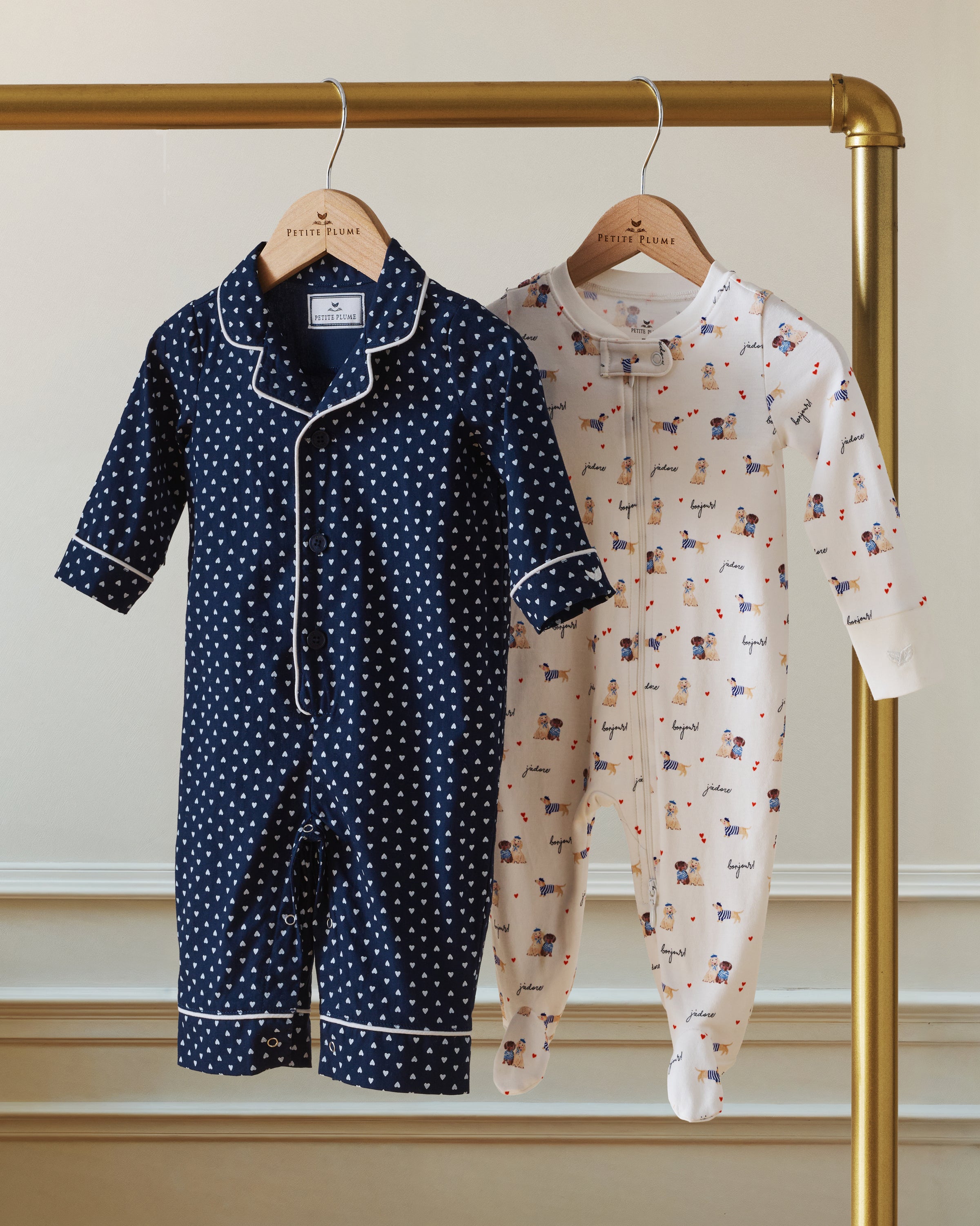 The Baby's Twill Classic Romper in Midnight Hearts is a navy blue onesie with long sleeves and legs, featuring a white heart pattern and white piping on the collar, cuffs, and front.