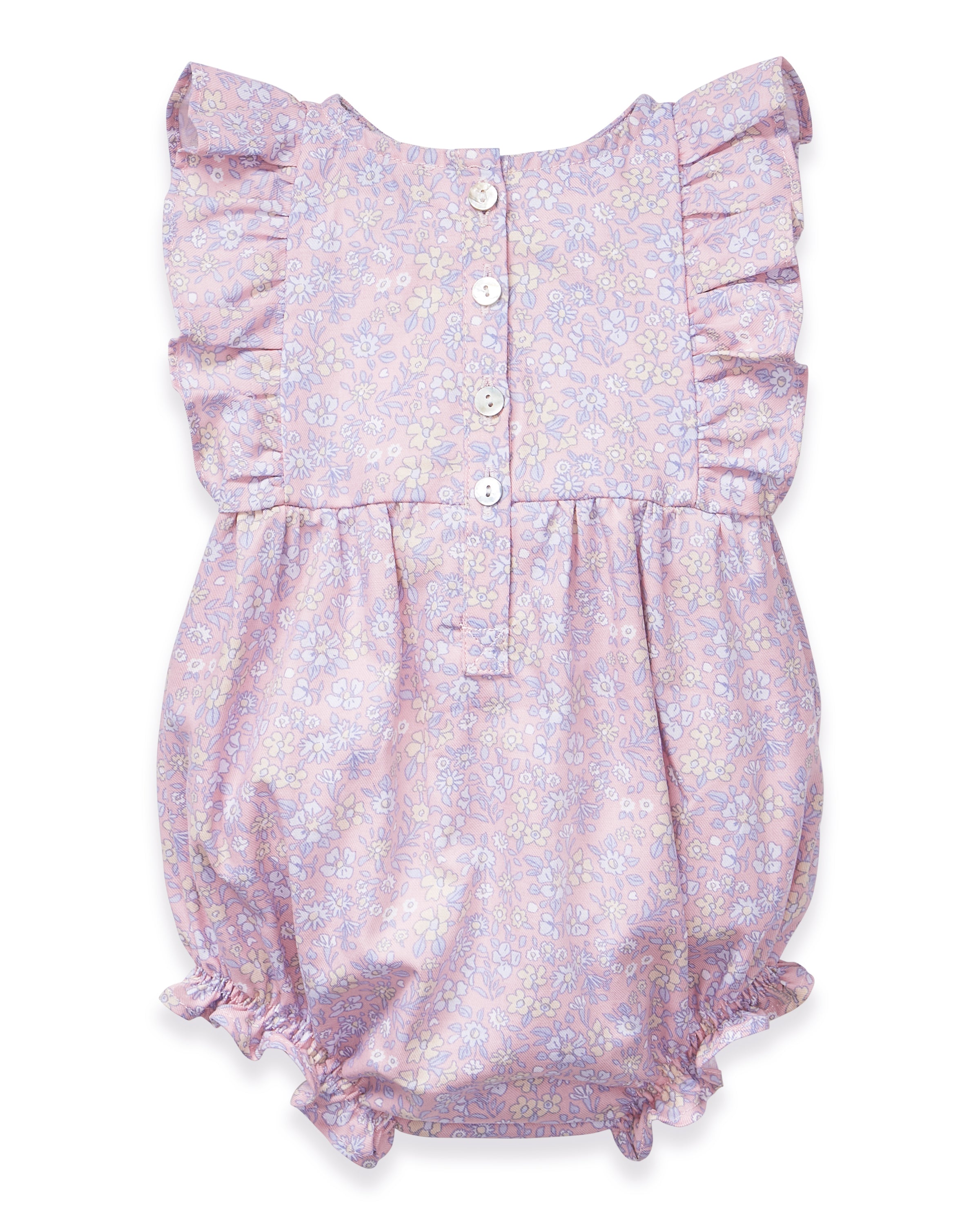 A curly-haired toddler stands barefoot, pointing left and looking that way, wearing the Baby's Twill Ruffled Romper in Fleur Blush against a plain light background.