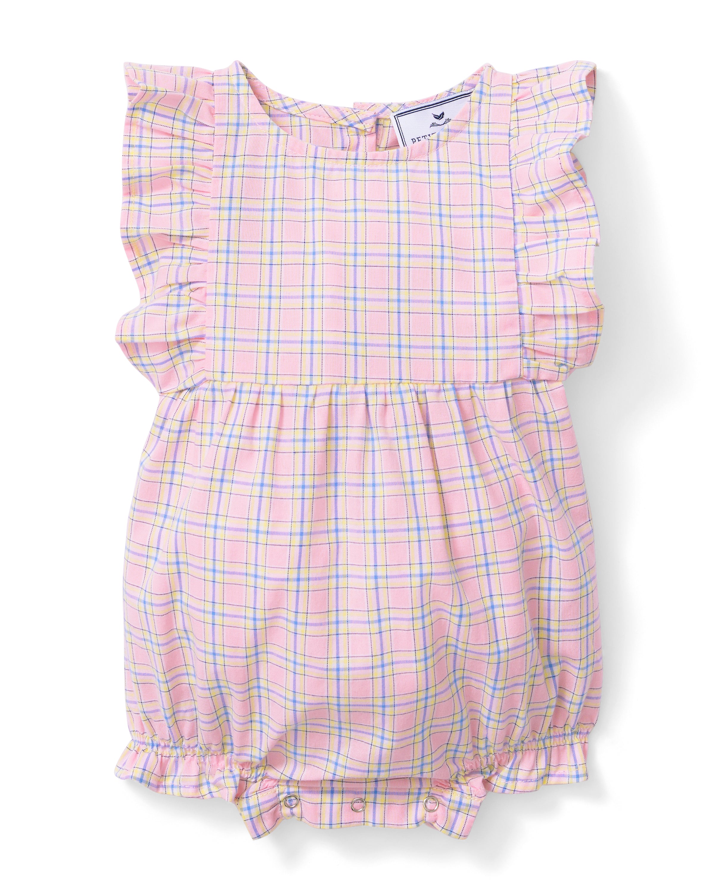 A toddler with curly hair wears the Baby's Twill Ruffled Romper in Peony Plaid, featuring ruffled sleeves, standing barefoot against a plain light background and looking slightly to the side.