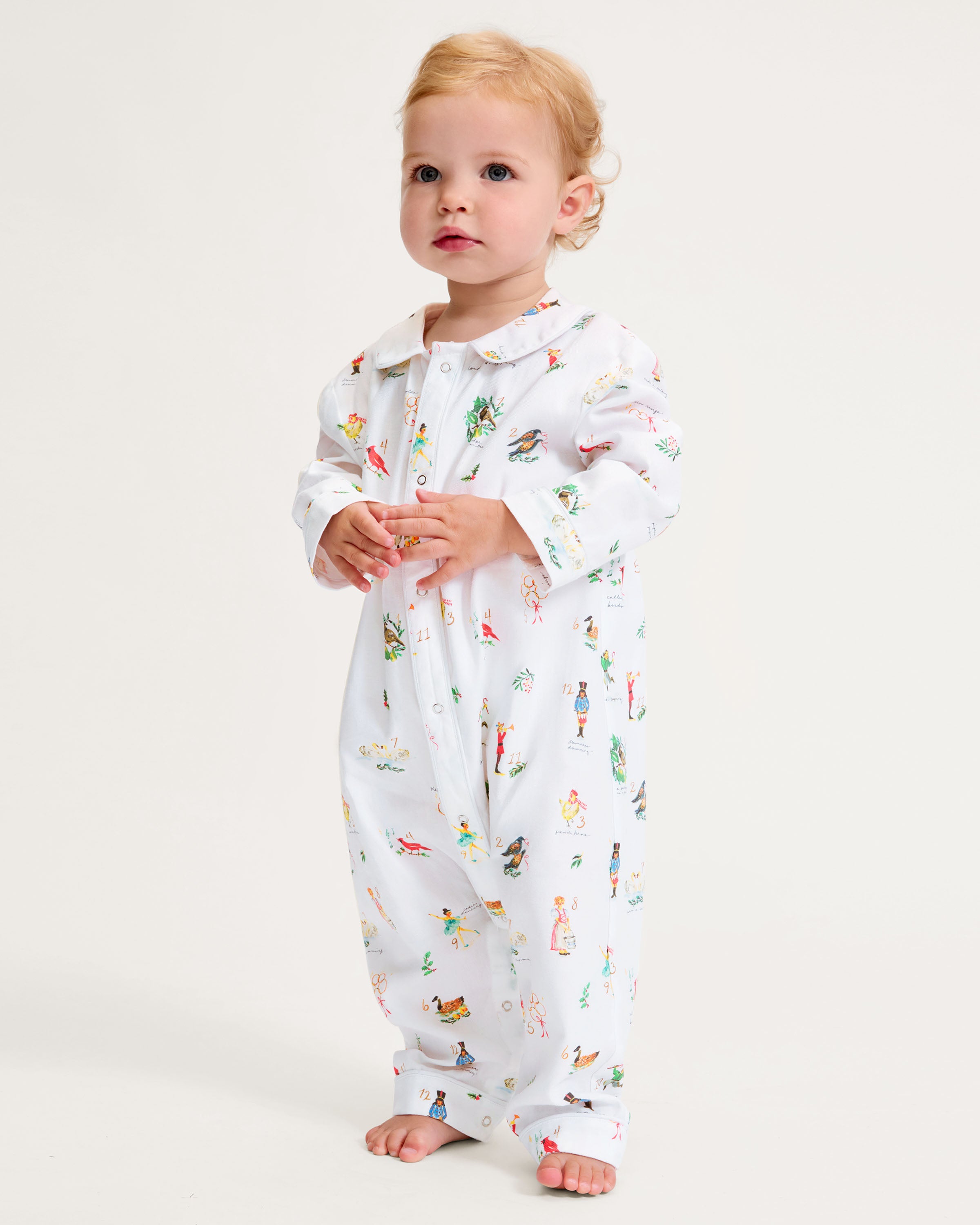 The Baby's Twill Cambridge Romper in 12 Days of Christmas features a white long-sleeve design with a collar, playful festive illustrations, and convenient snap buttons down the front and legs.