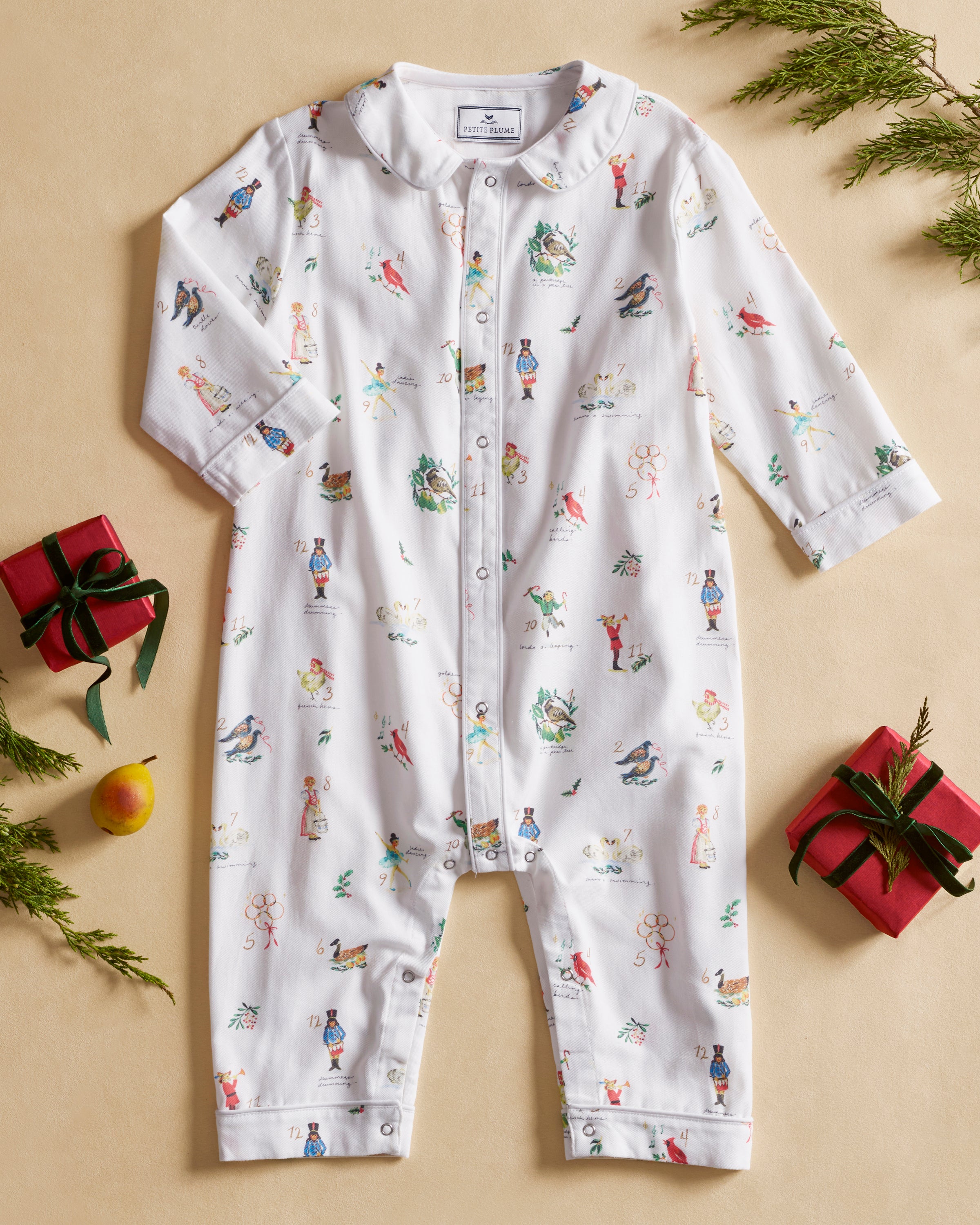 The Baby's Twill Cambridge Romper in 12 Days of Christmas features a white long-sleeve design with a collar, playful festive illustrations, and convenient snap buttons down the front and legs.