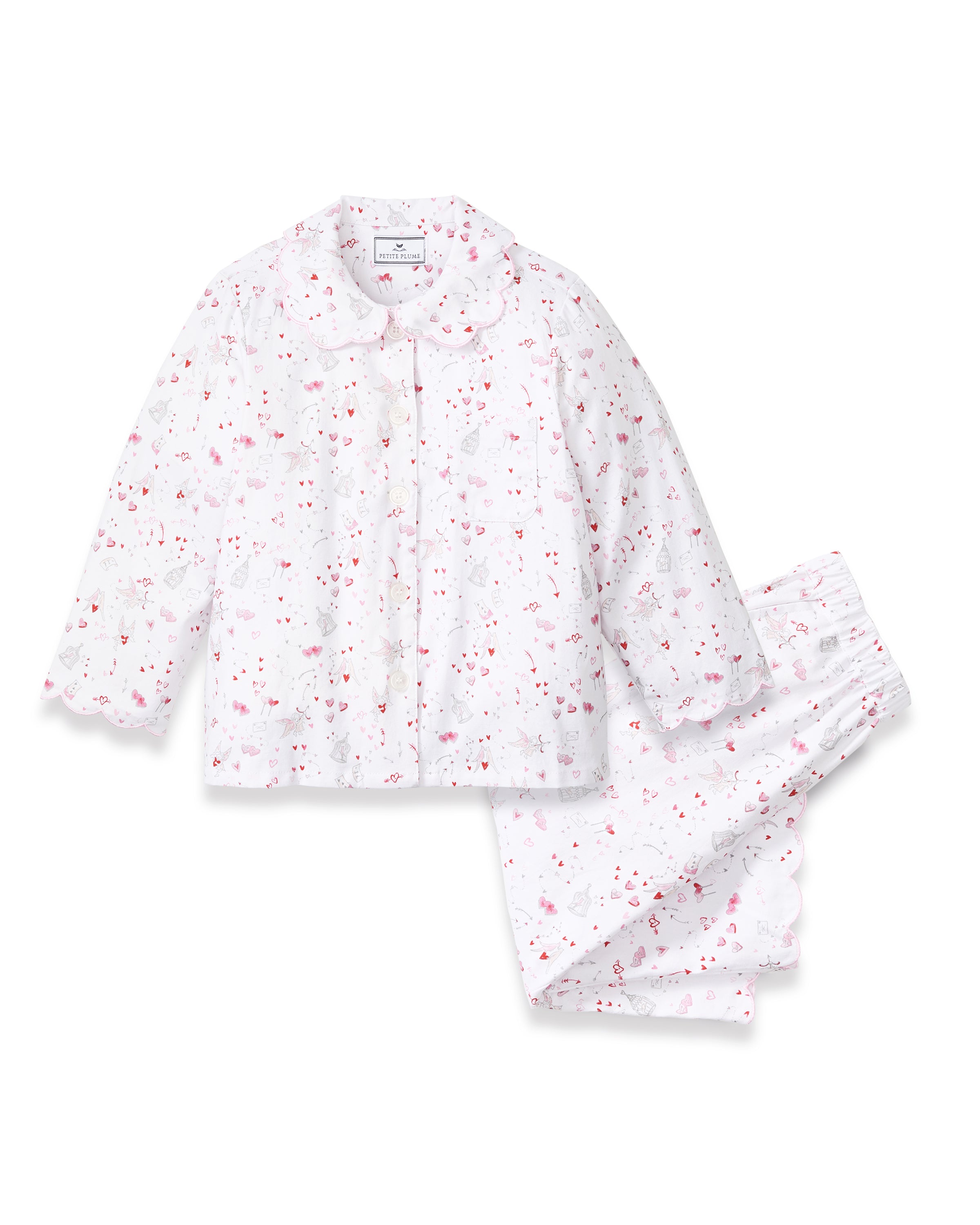 The Kid's Twill Colette Pajama Set in Love Song features white pajamas with a scalloped collar and cuffs, adorned with pink and red heart and dot patterns. The set includes a long-sleeved button-up top and matching pants.