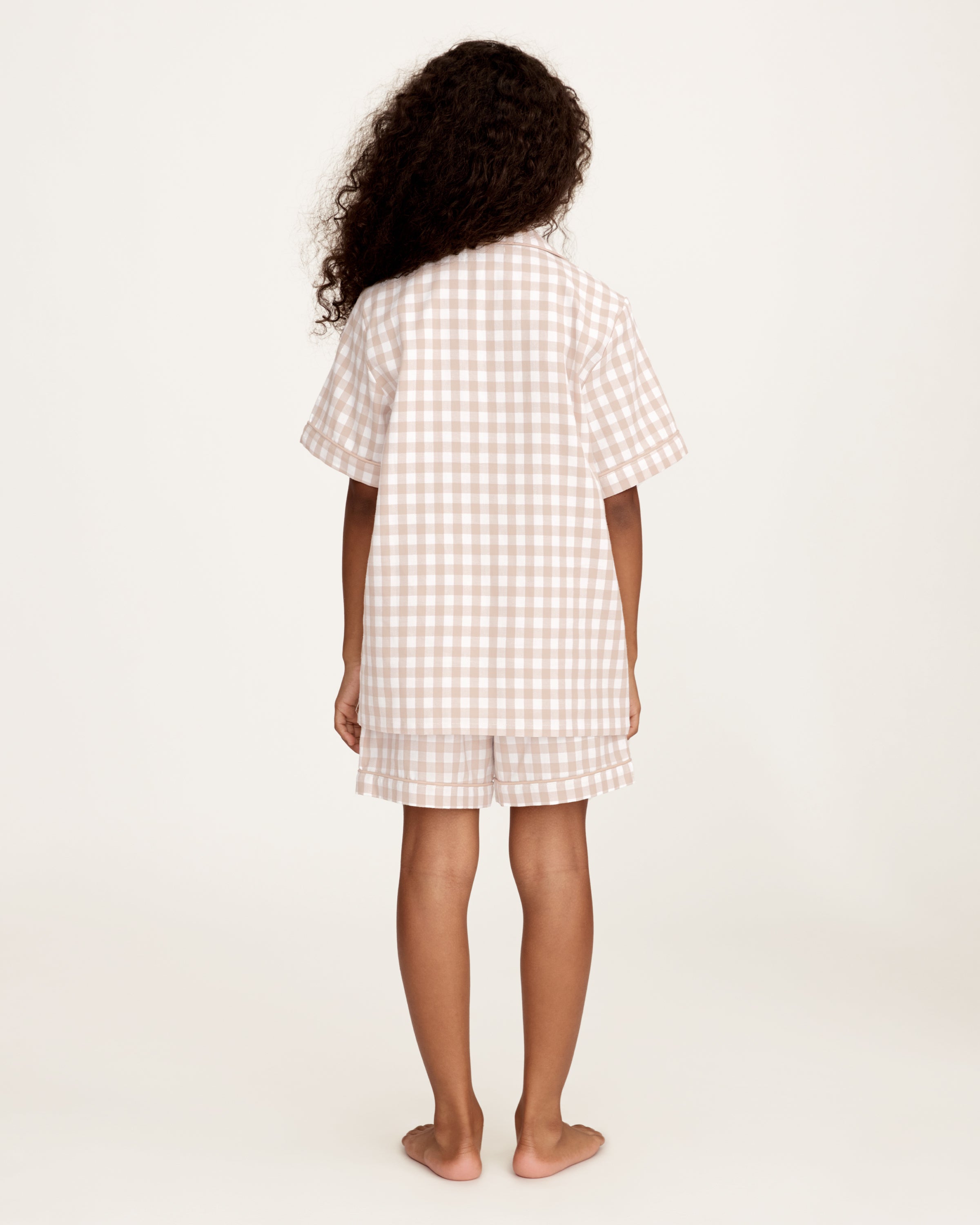 The Kid's Twill Pajama Short Set in Camel Gingham features a light beige and white gingham pattern with a collared, button-front top, chest pocket, and elastic waist shorts.