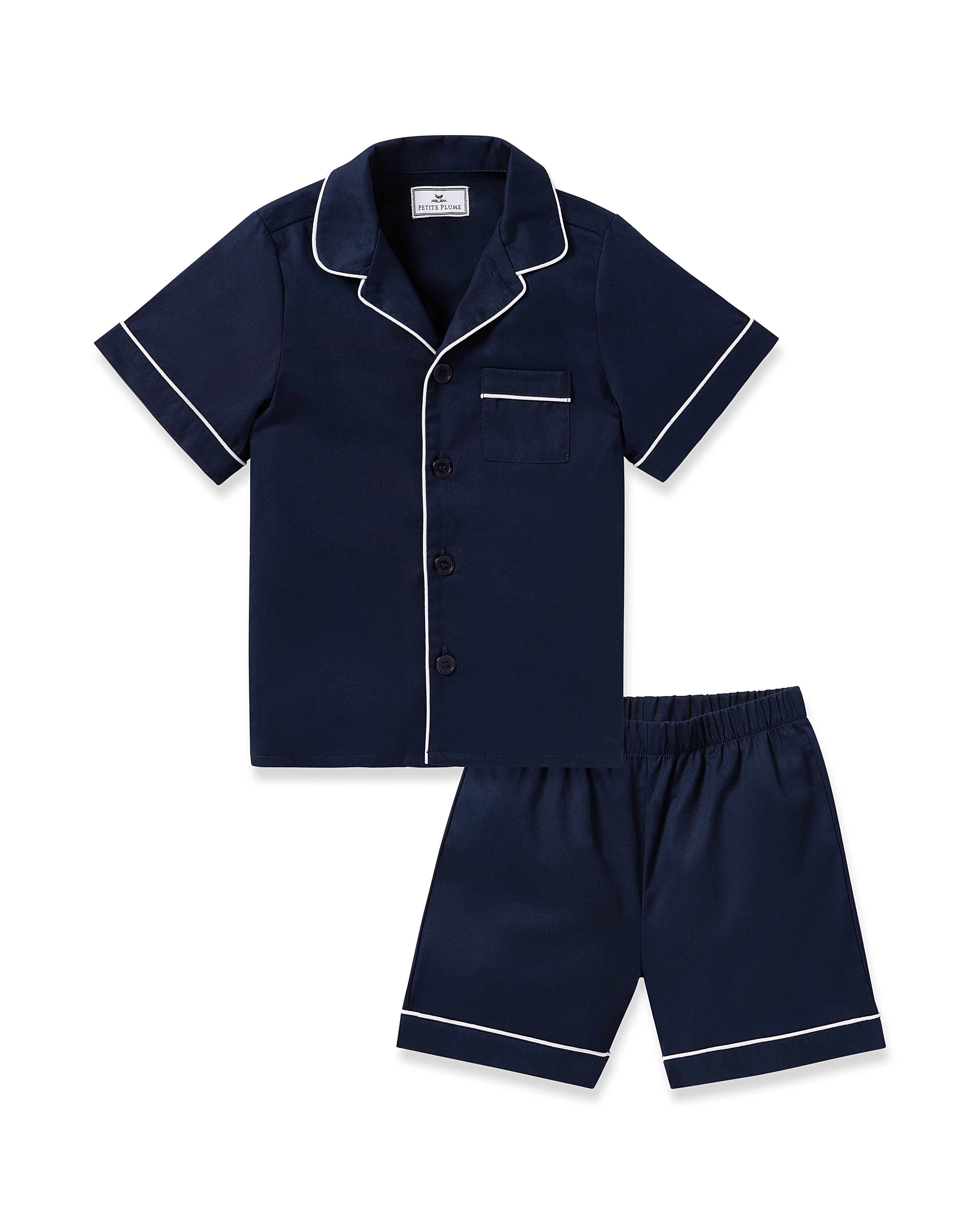 Experience luxurious sleepwear with the Kids Twill Short Sleeve Short Set in Navy by Petite Plume, featuring white piping, a button-up top with a chest pocket, and matching shorts made from inherently flame-retardant fiber for comfort and peace of mind.
