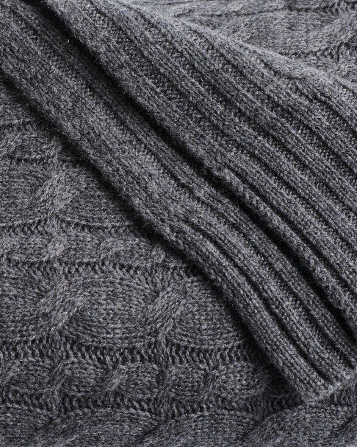 Close-up of Petite Plumes Cashmere Cable Knit Throw in Dark Grey featuring a ribbed texture on the right and a subtle diamond pattern on the left. The soft, thick material is perfect for crafting cozy sweaters or stylish home decor, making it a giftable choice.