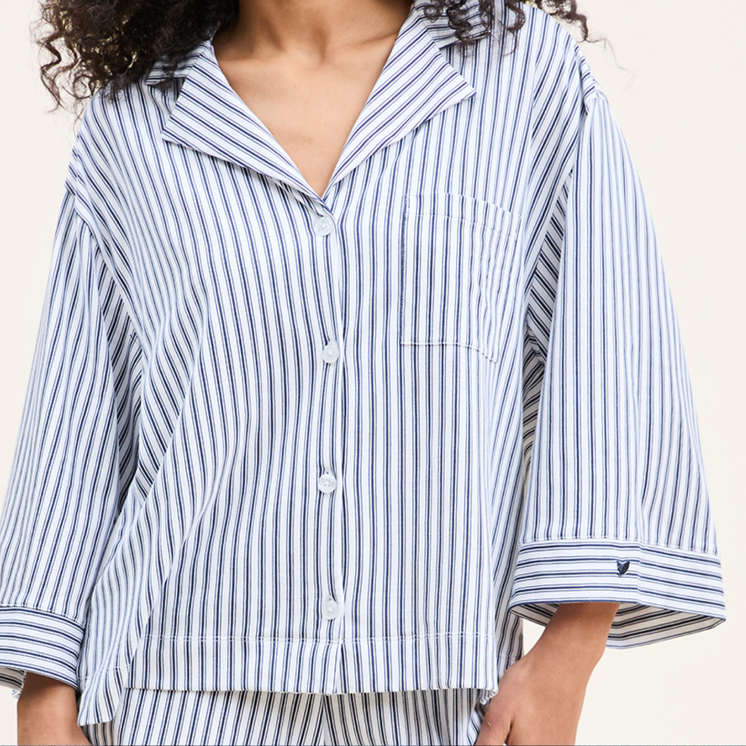A person wearing a loose-fitting, long-sleeved, blue and white vertically striped pajama top with buttons down the front and a chest pocket. Only the upper body is visible.