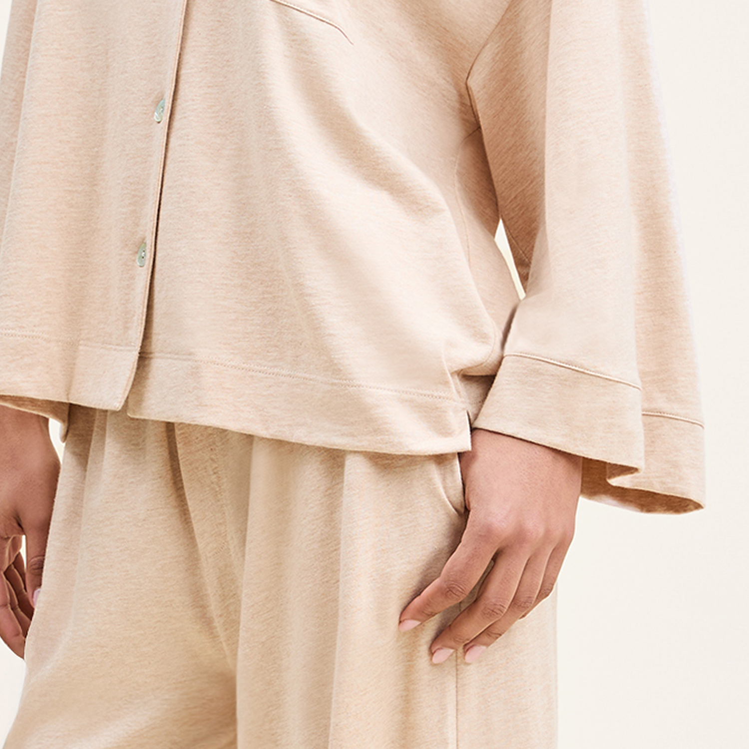 A person wearing a loose-fitting, long-sleeve beige top and matching beige pants, with one arm relaxed by their side. The outfit appears soft and comfortable.