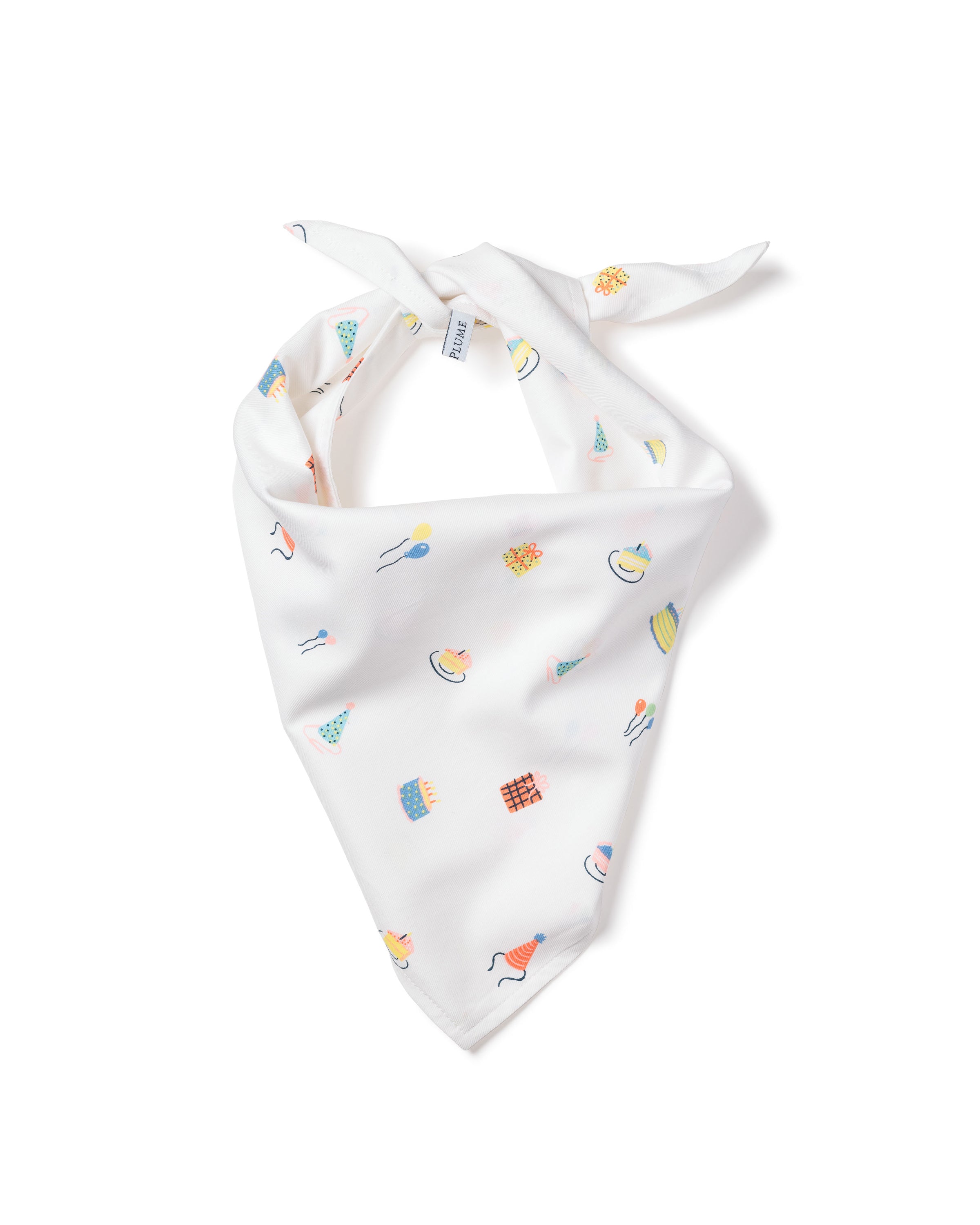 A fluffy white dog with pointed ears sits on a wooden floor, wearing a charming Dog Twill Bandana in Birthday Wishes by Petite Plume. The adorable accessory complements the dogs joyful expression as it looks up with an open mouth, tongue out, appearing to smile.