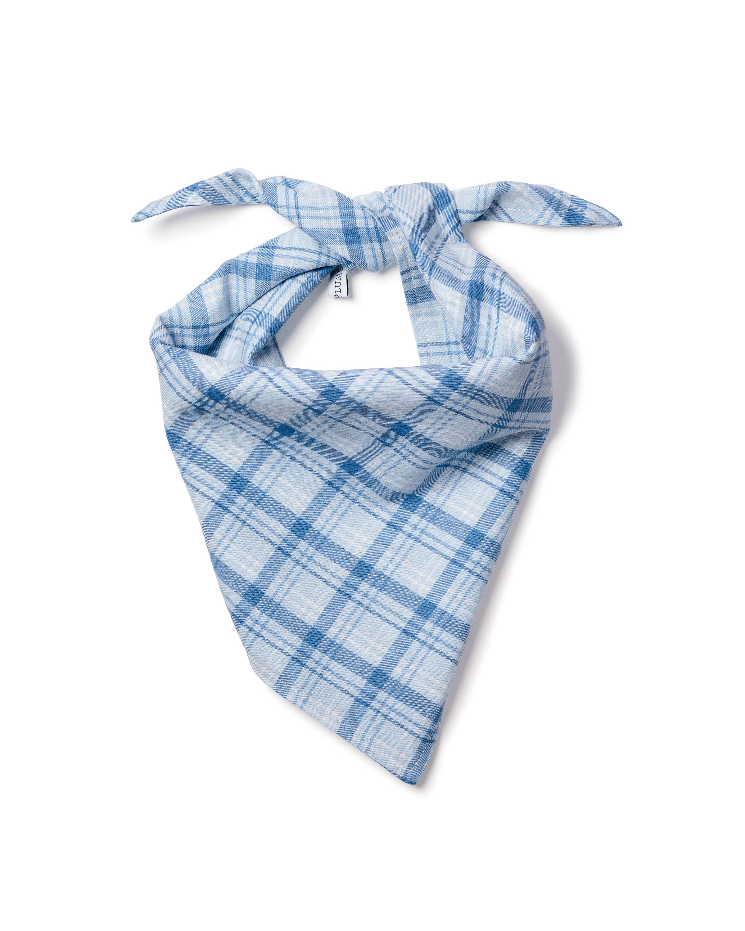 A fluffy white dog with pointy ears sits on a wooden floor, donning a charming Dog Twill Bandana in Seafarer Tartan from Petite Plume. With an open mouth and cheerful expression, the pup looks directly at the camera, adding warmth to the scene.