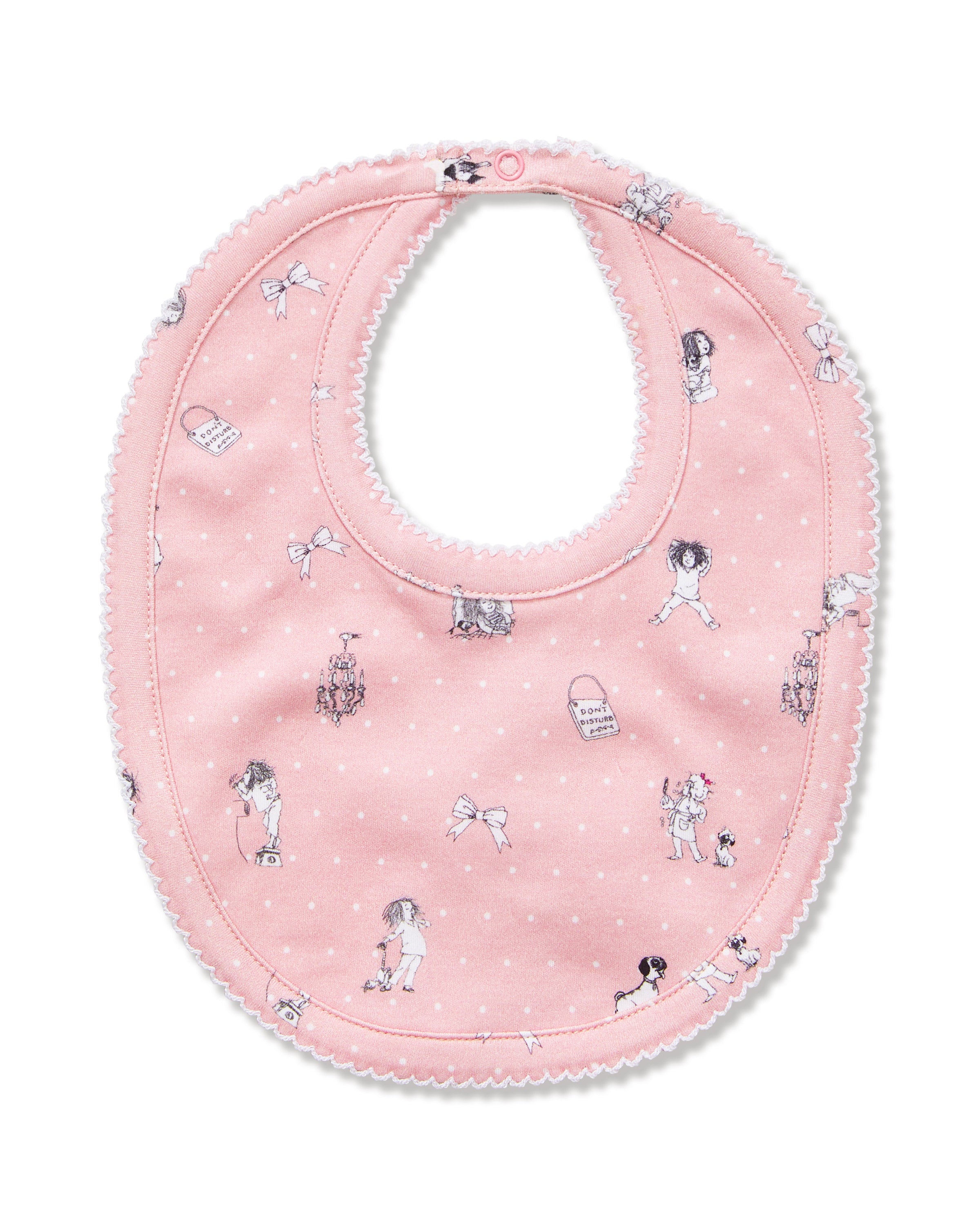 The Petite Plume x Eloise Baby Pima Bib in Eloise Adventures features pink fabric with white polka dots, playful black-and-white drawings, whimsical motifs, a scalloped edge, and a convenient snap closure at the neck.