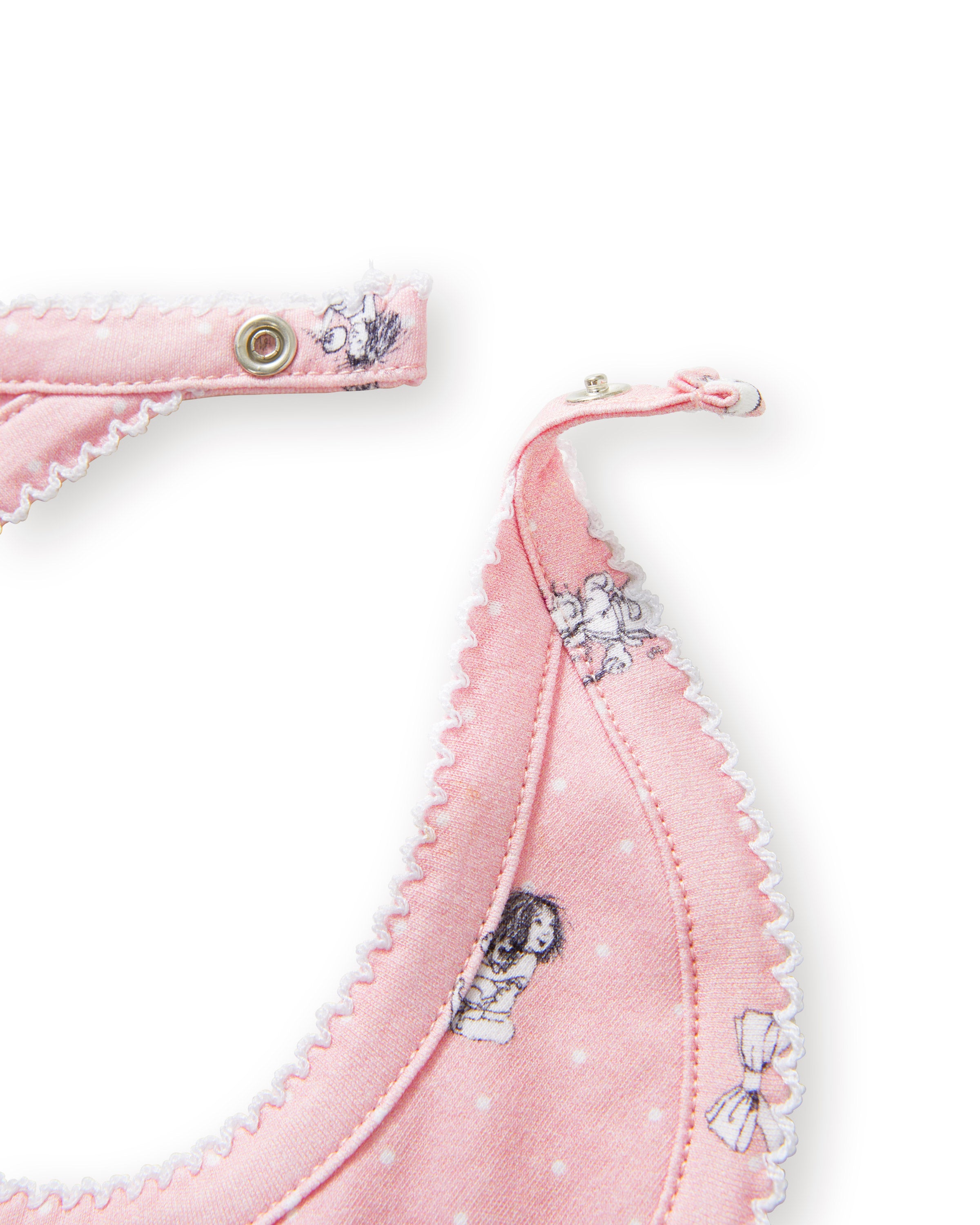 The Petite Plume x Eloise Baby Pima Bib in Eloise Adventures features pink fabric with white polka dots, playful black-and-white drawings, whimsical motifs, a scalloped edge, and a convenient snap closure at the neck.
