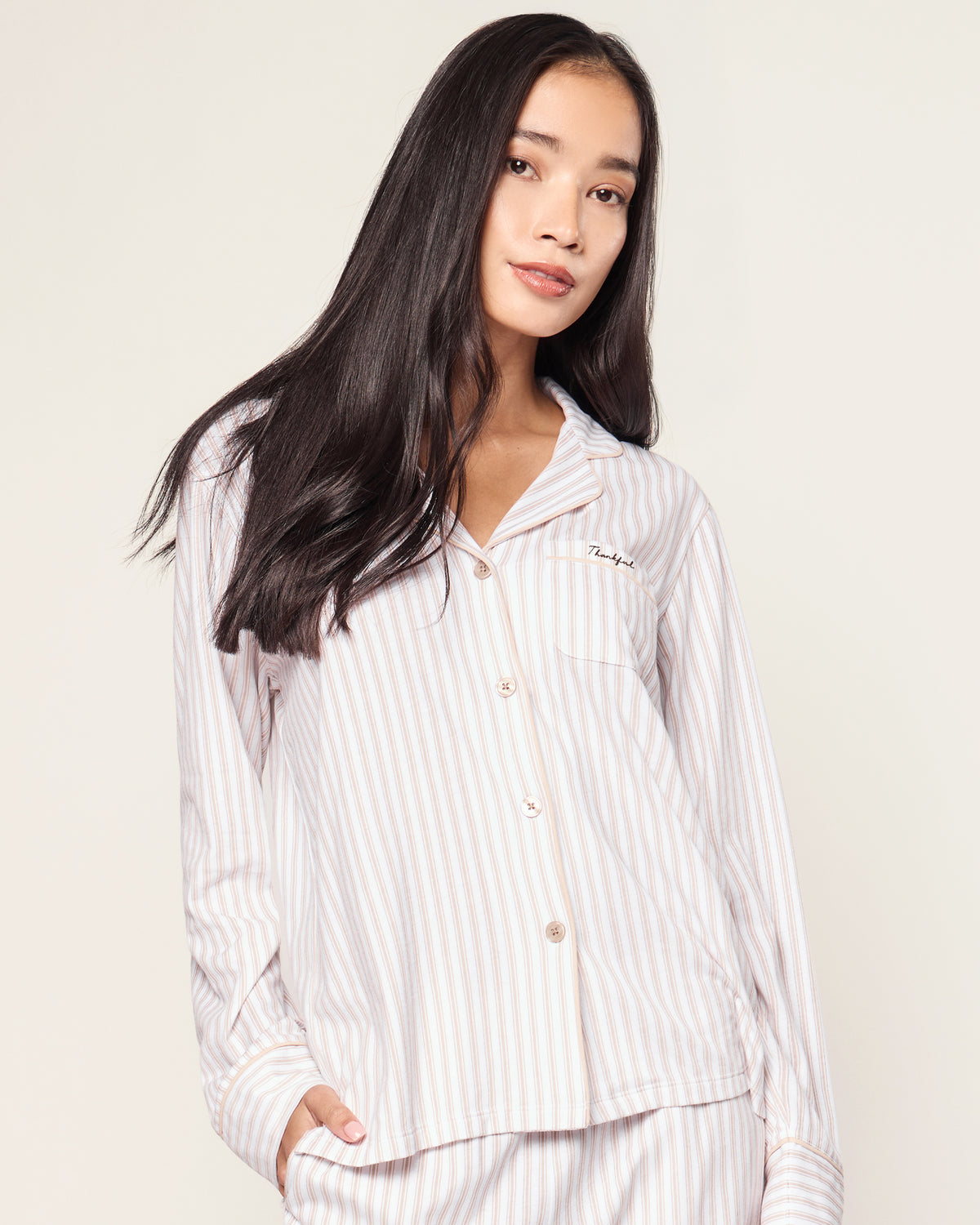 The Women's Pima Pajama Set in Camel Ticking with "Thankful" embroidery features a beige and white striped, long-sleeve button-up top with a chest pocket and matching elastic-waist pants, shown neatly arranged on a white background.