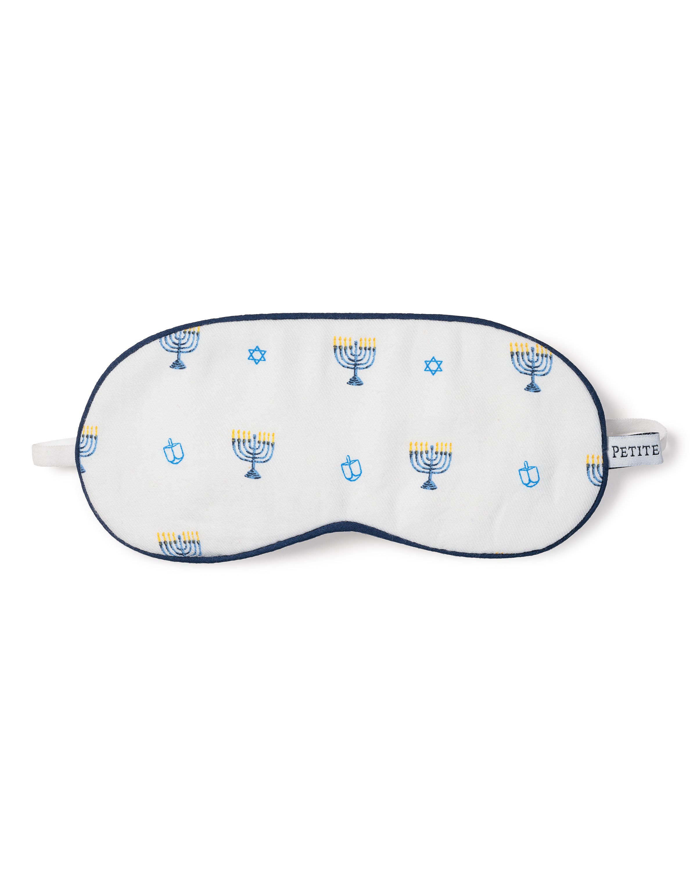 The Kids Twill Sleep Mask in Happy Hanukkah by Petite Plume, in white with blue trim, showcases menorahs, Stars of David, and dreidels—ideal for pairing with your Hanukkah pajamas. A small side label says PETITE.