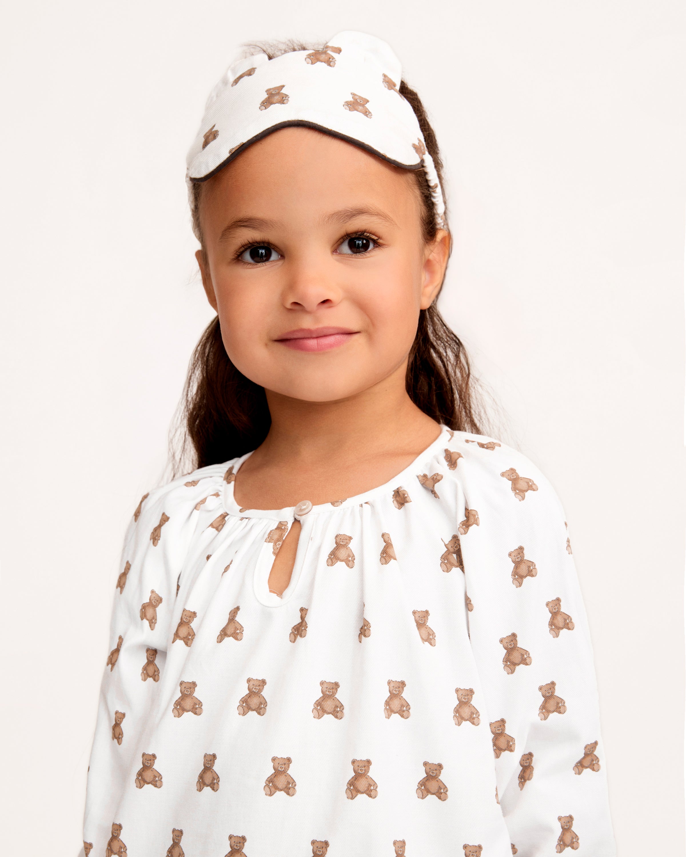 The Kid's Twill Sleep Mask in Teddy Tales features a white design with small brown teddy bear prints, two ear-shaped accents at the top, and a PETITE tag on the right side.