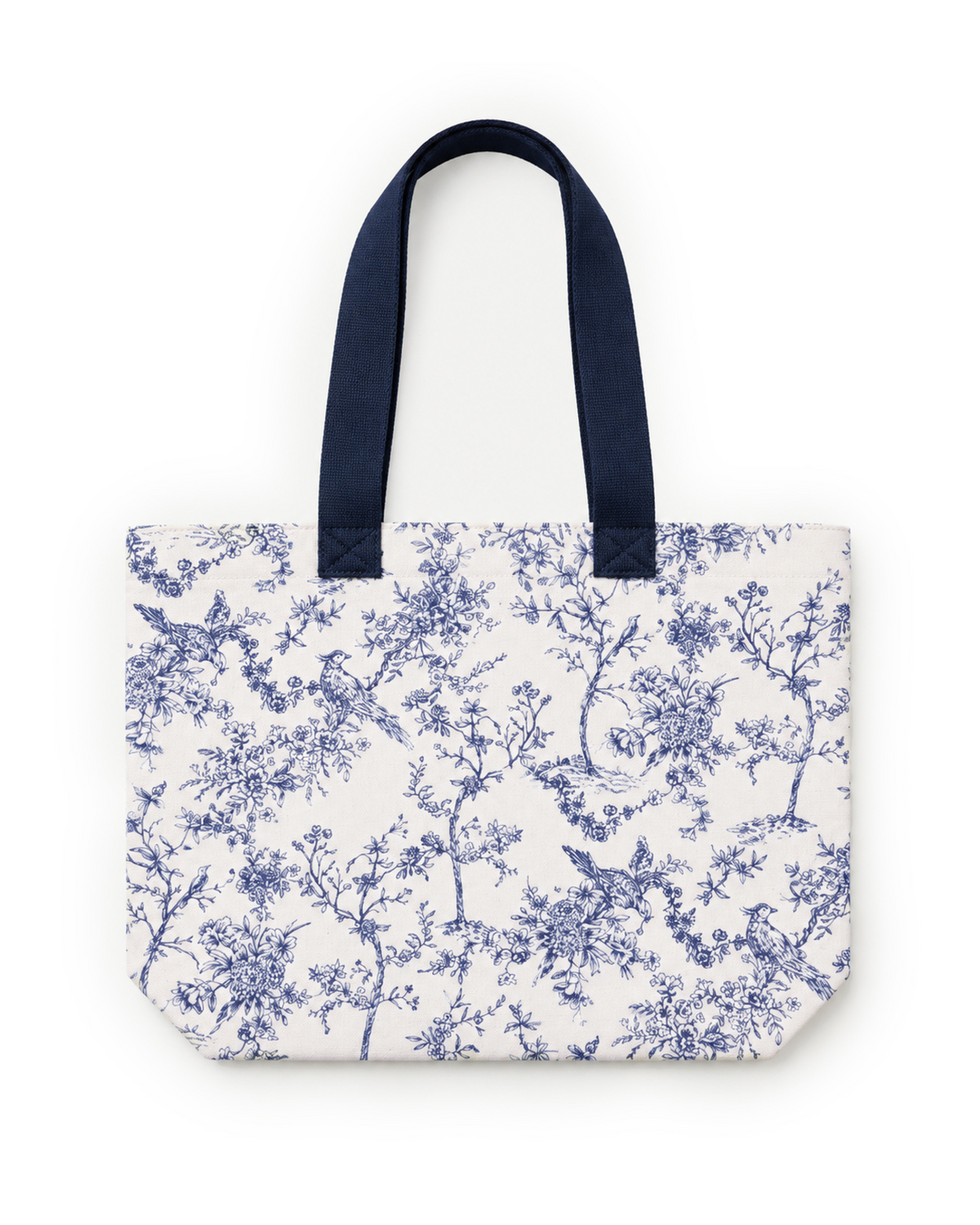 The Timeless Toile Tote Bag features blue handles and a blue toile pattern with birds, tree branches, and flowers. It is photographed against a white background.