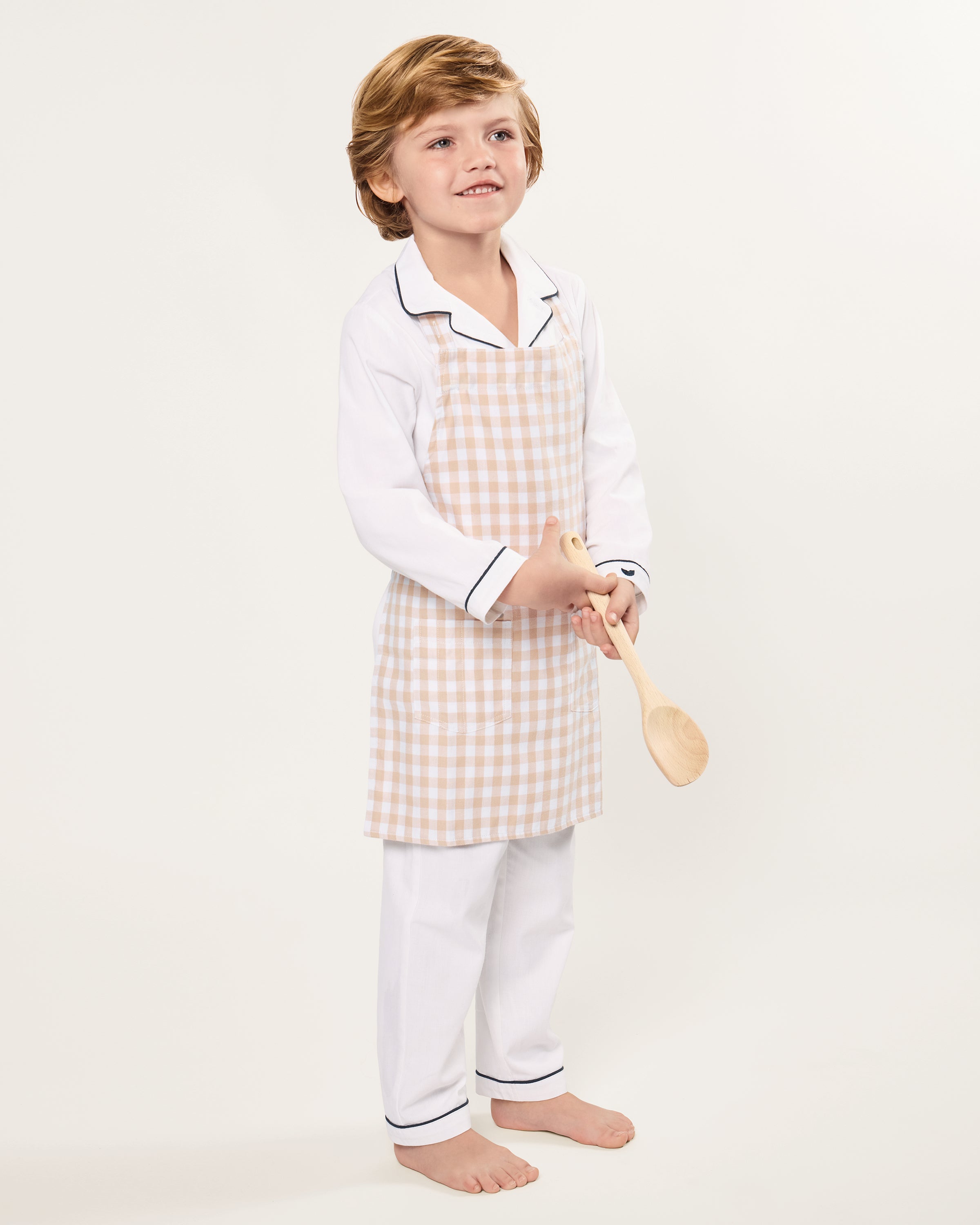 The Kid's Twill Apron in Camel Gingham, featuring a beige and white gingham pattern, two front pockets, and long waist ties, is displayed on a white background.