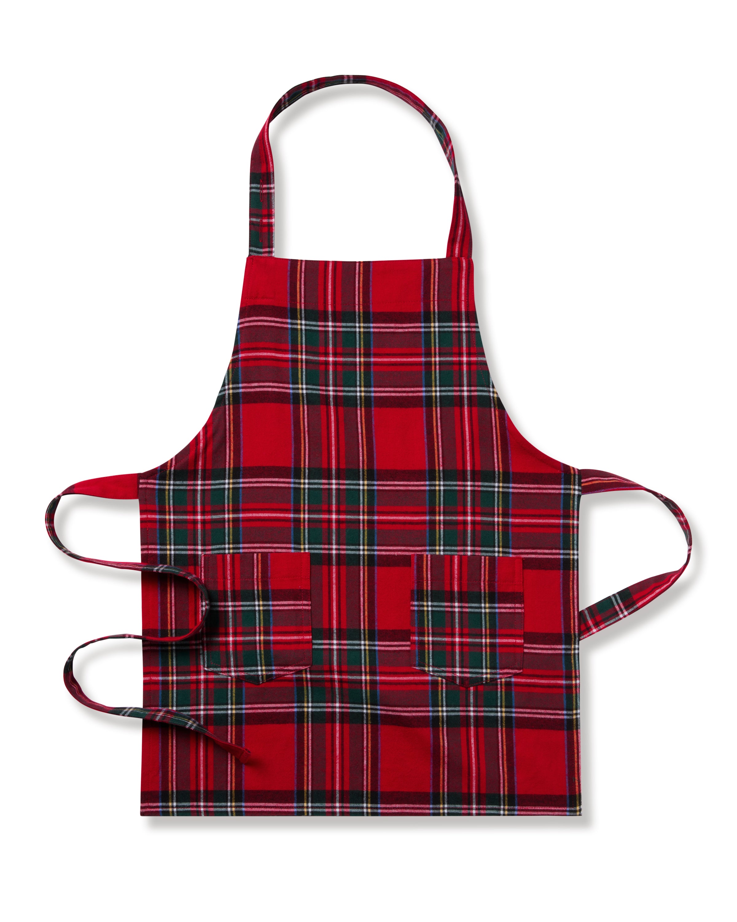Two Petite Plume Kids Aprons in Imperial Tartan with pockets hang on a wooden peg rack, alongside a white dish towel with red and black patterns. A wooden spoon and spatula peek from one apron pocket, perfect for holiday baking against a light brown backdrop.