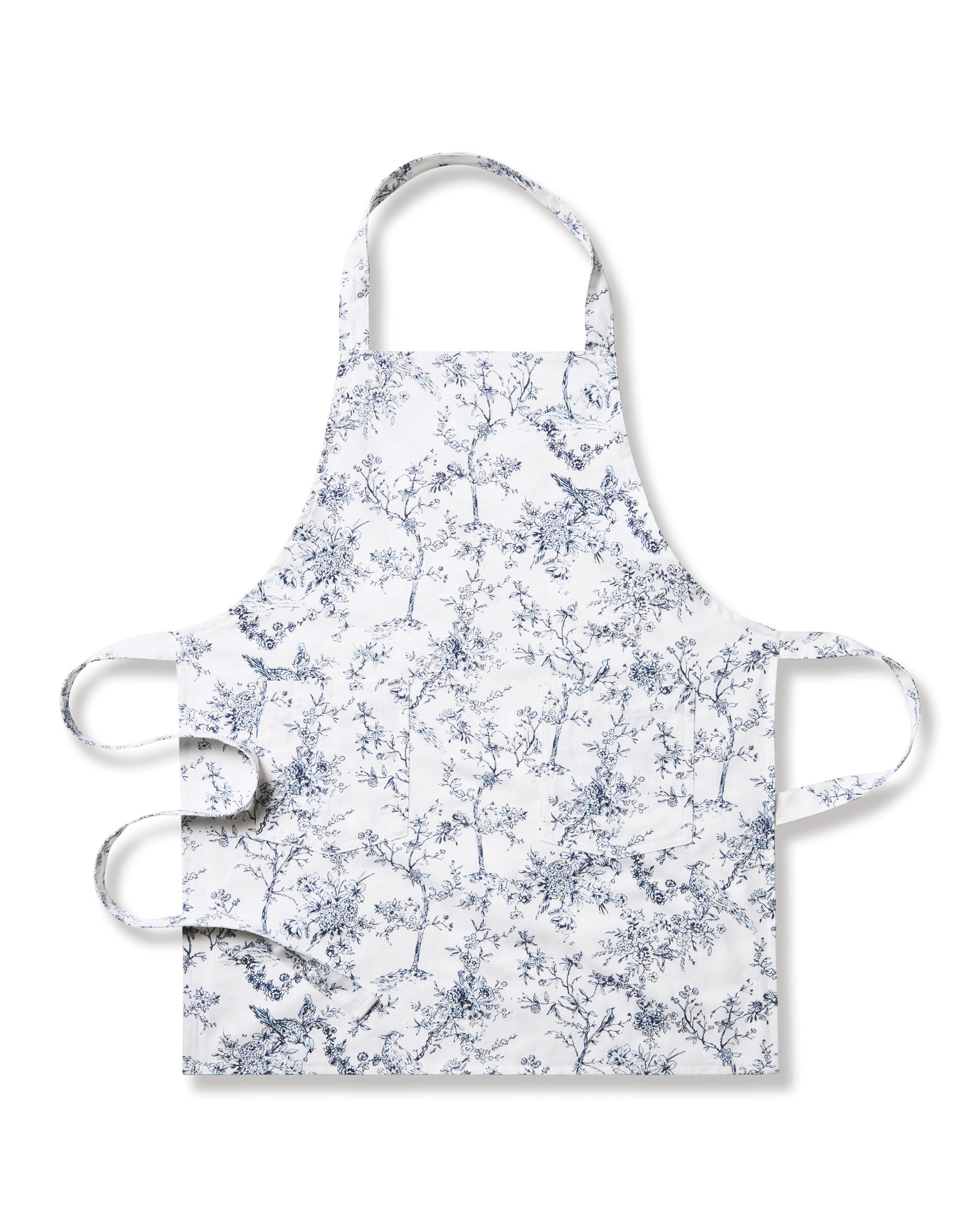 A child in a Petite Plume blue long-sleeve shirt and a Kids Apron in Timeless Toile stands facing forward against a plain backdrop, prepared for delightful holiday baking.