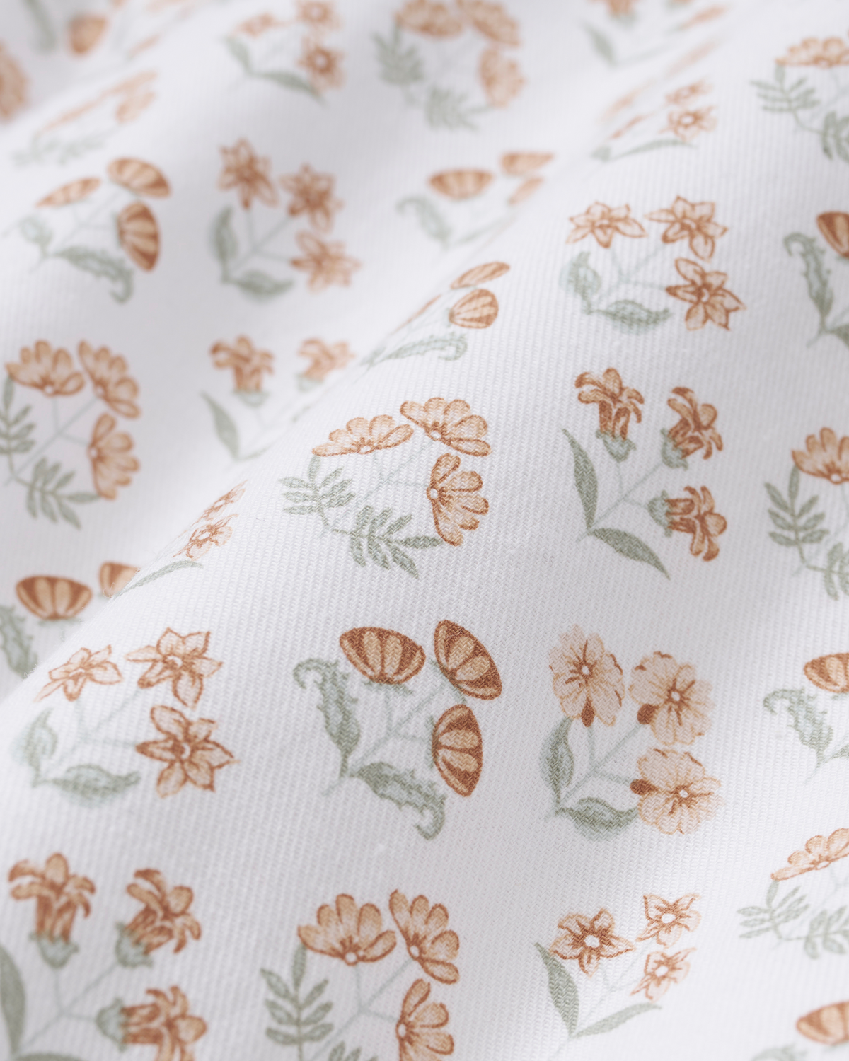 The Luxe Premium Percale Bed Sheets in Estate Garden feature a white fabric adorned with a delicate floral and mushroom pattern in soft brown and green tones. Subtle surface folds create texture, adding depth and dimension to the gentle botanical print.