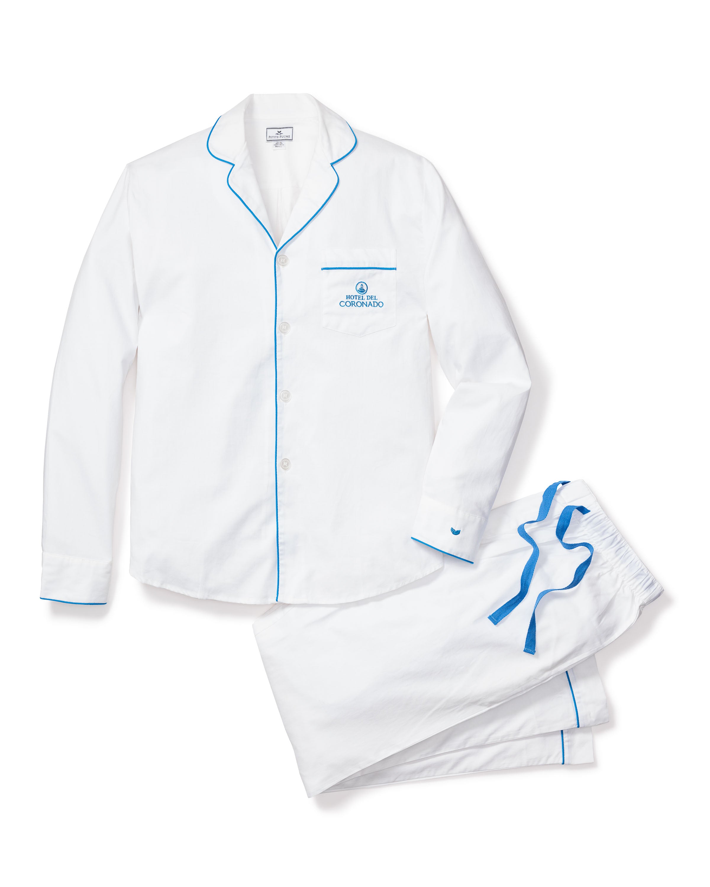 Petite Plumes Mens Twill Pajama Set, in collaboration with Hotel del Coronado, offers a luxurious white ensemble featuring blue piping. The set includes a long-sleeve button-up top with an embroidered logo and drawstring pants with a blue waist ribbon, showcasing timeless charm.