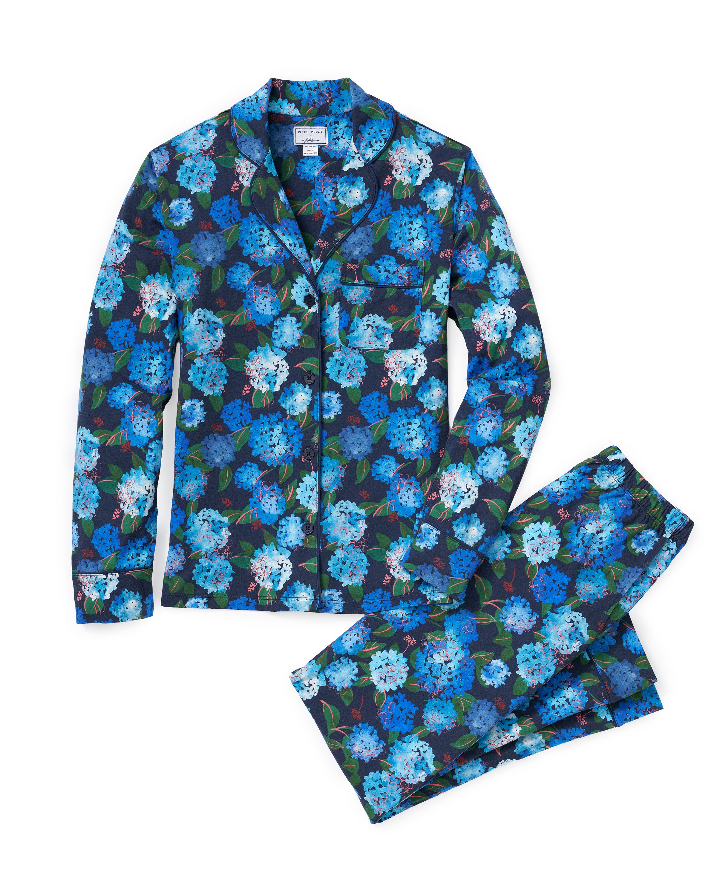 Petite Plume x Hedges Women’s Pima Pajama Set in Hydrangea features a two-piece design with a collared, button-up top and matching pants, both adorned with a blue floral pattern showcasing leaves and an array of blue, teal, and white flowers.