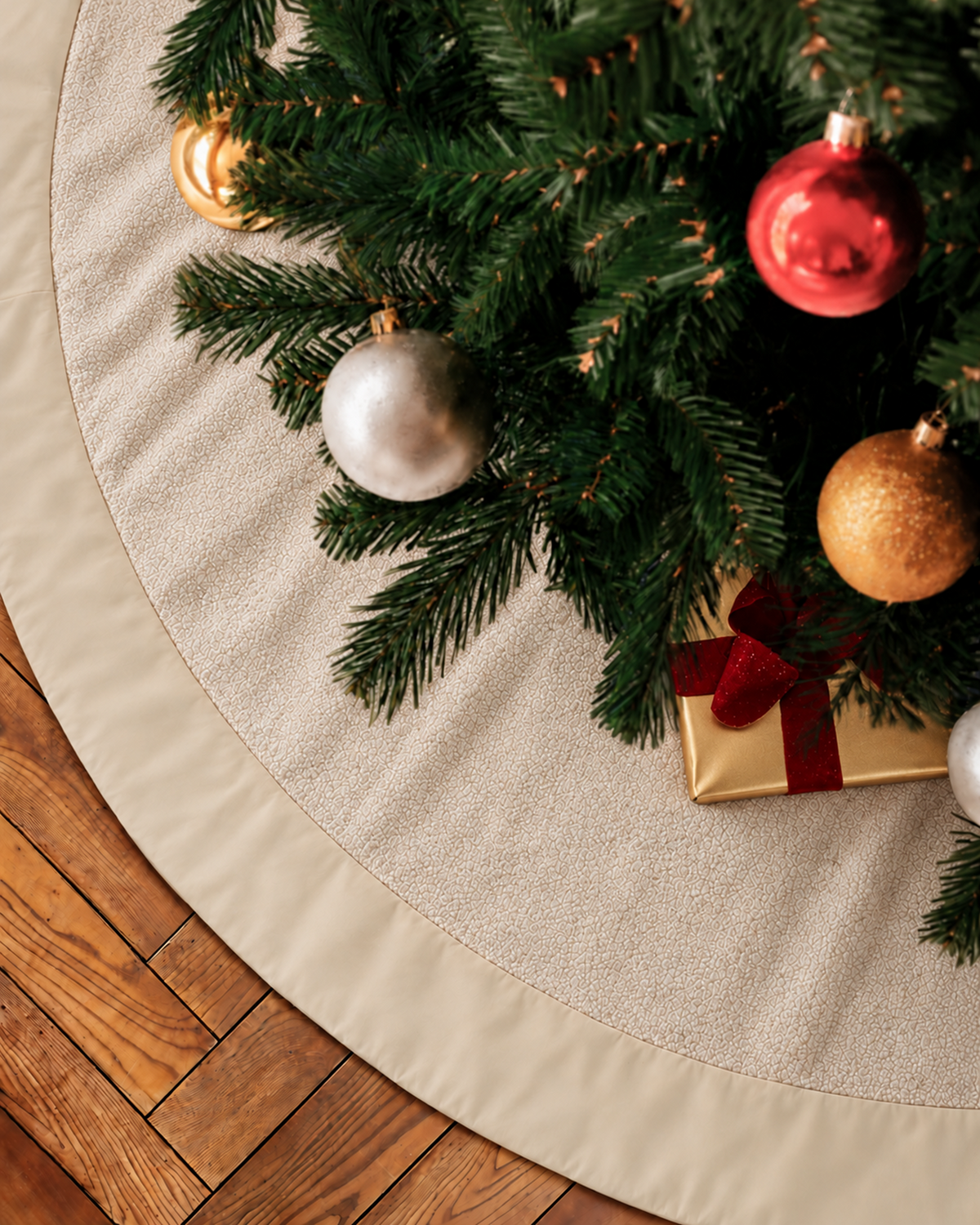 A textured, cream-colored Boucle Christmas Tree Skirt in Cream with a smooth border placed under a decorated Christmas tree on a wood floor.