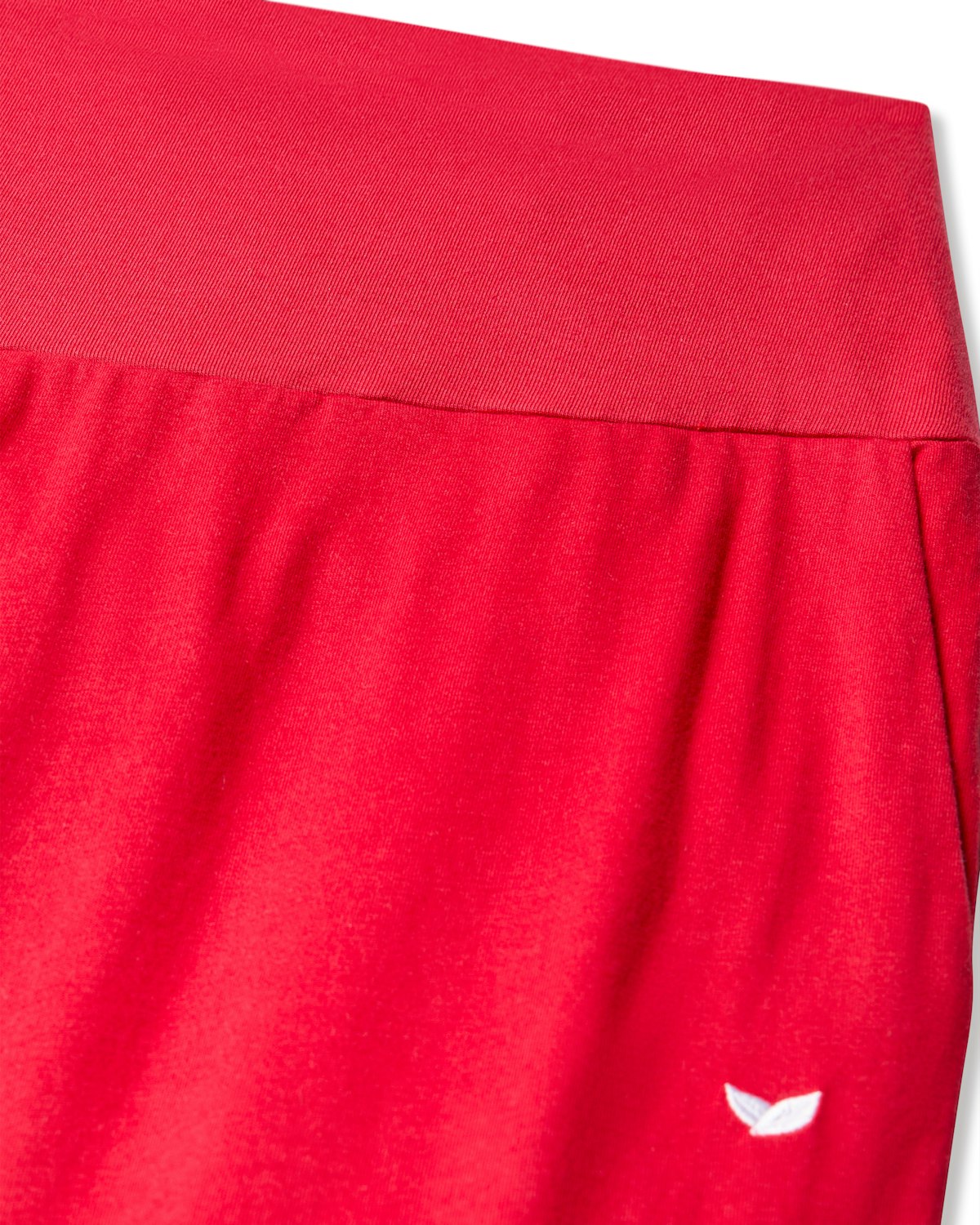 Close-up of Petite Plume Womens Pima Maternity Pants in Red featuring an elastic waistband and over the belly support band. A small white logo is near the bottom right corner. The smooth, lightweight fabric ensures comfort ideal for maternity wear.